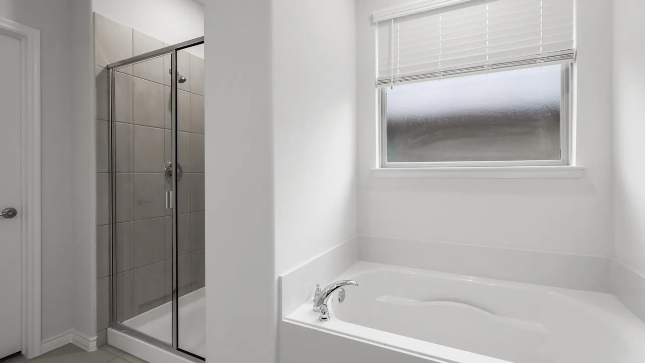 Sleek bathroom featuring a built-in soaking tub with a chrome faucet, a glass-enclosed shower with gray tile surround, and a window with horizontal blinds