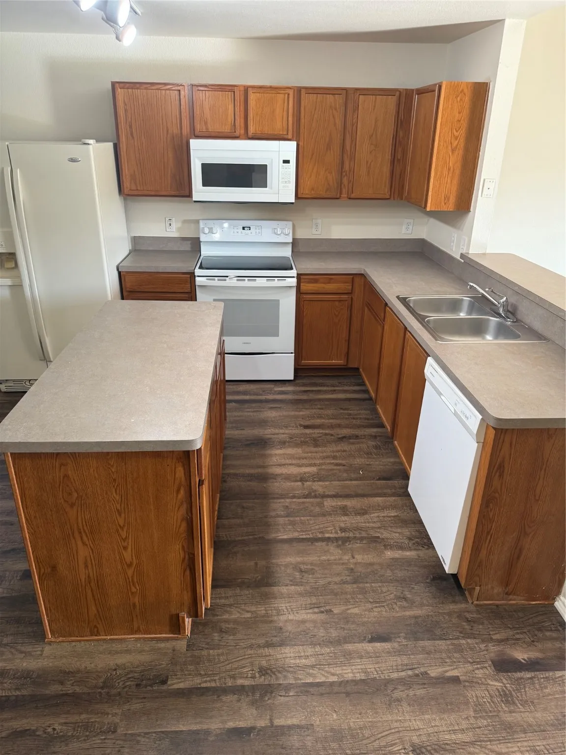 Kitchen with brown cabinets, white appliances, dark wood finished floors, and a center island