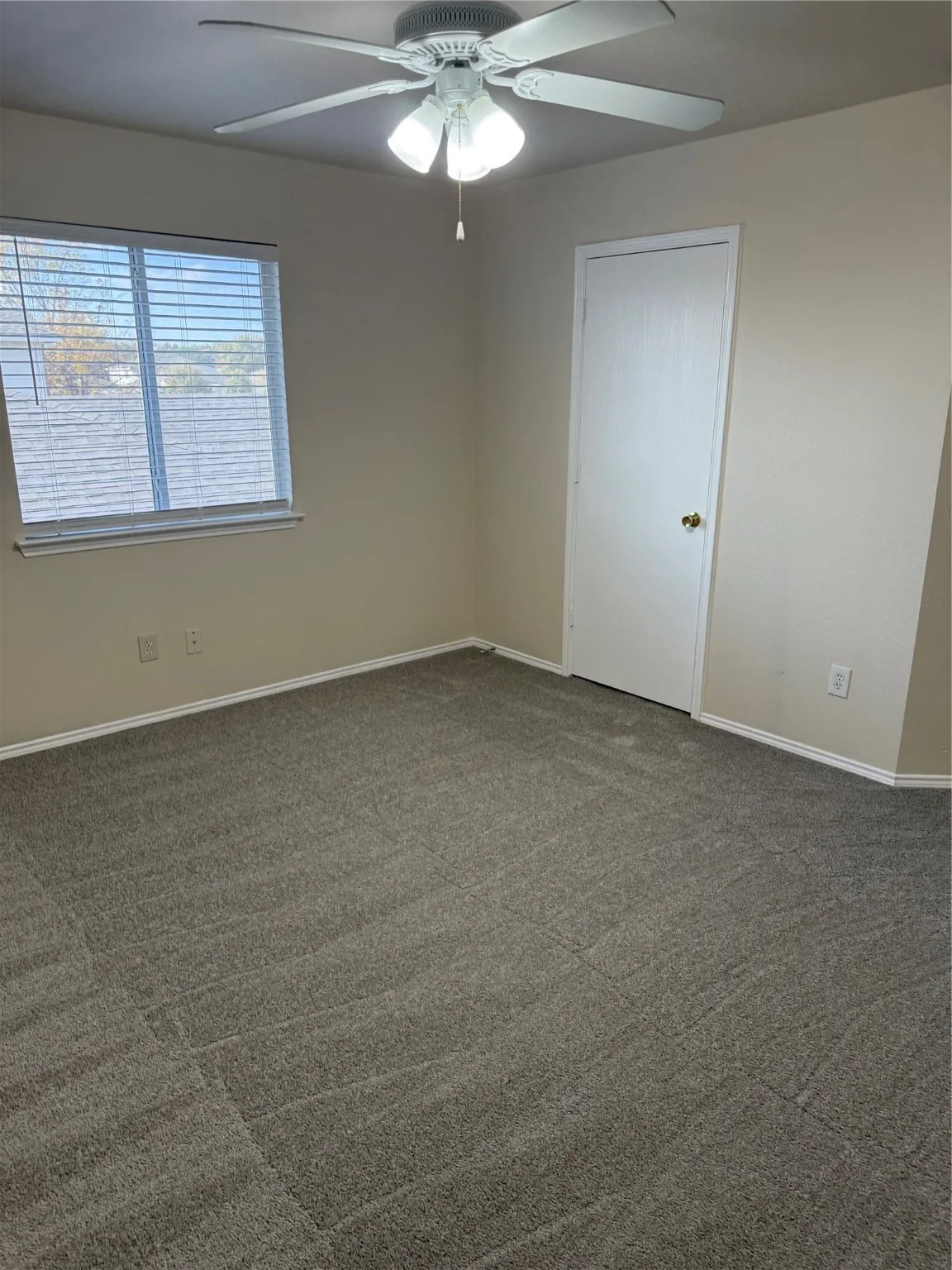 Empty room featuring a ceiling fan and dark colored carpet
