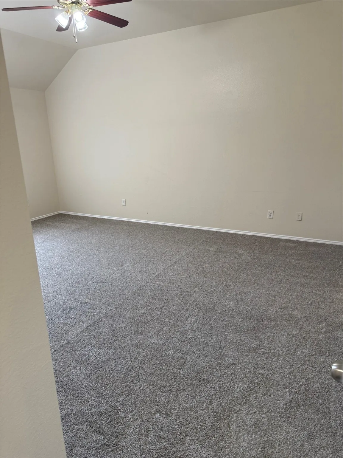 Spare room featuring dark carpet, lofted ceiling, and a ceiling fan