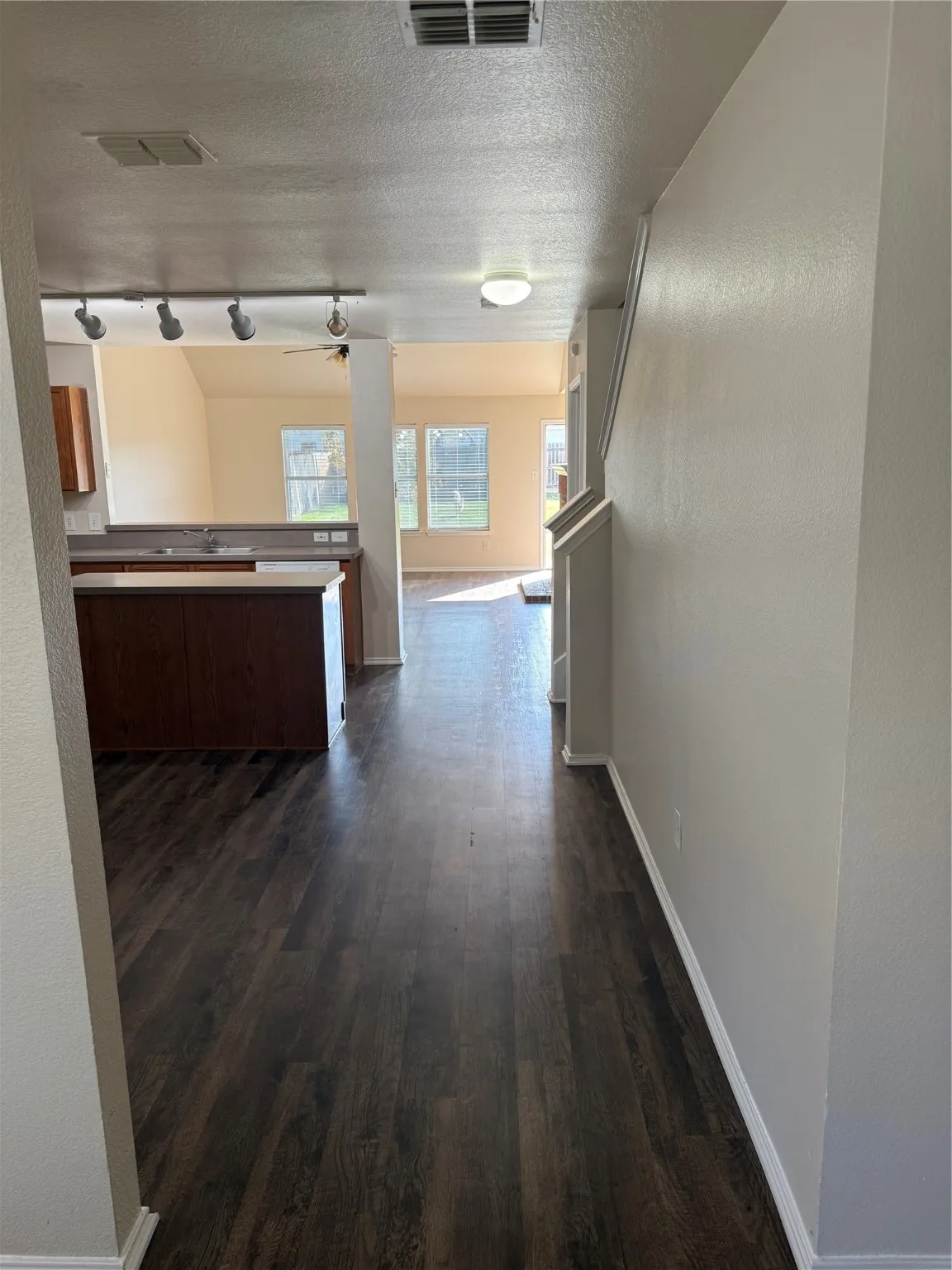 Corridor featuring a textured ceiling, dark wood finished floors, rail lighting, and a textured wall