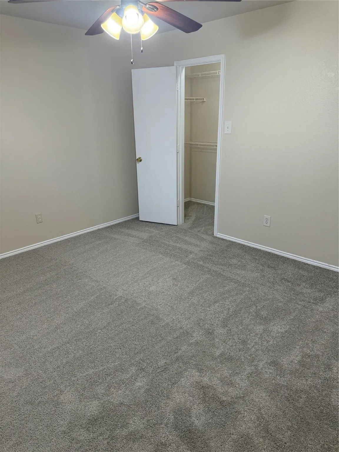 Unfurnished bedroom with ceiling fan, a spacious closet, and carpet flooring