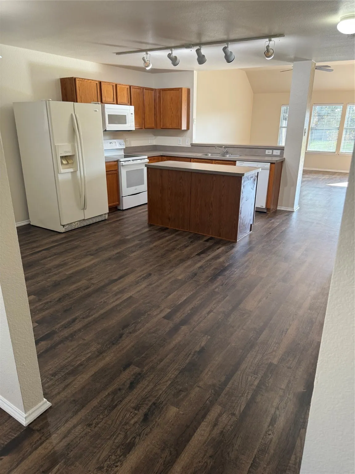 Kitchen with white appliances, brown cabinets, light countertops, and dark wood-type flooring