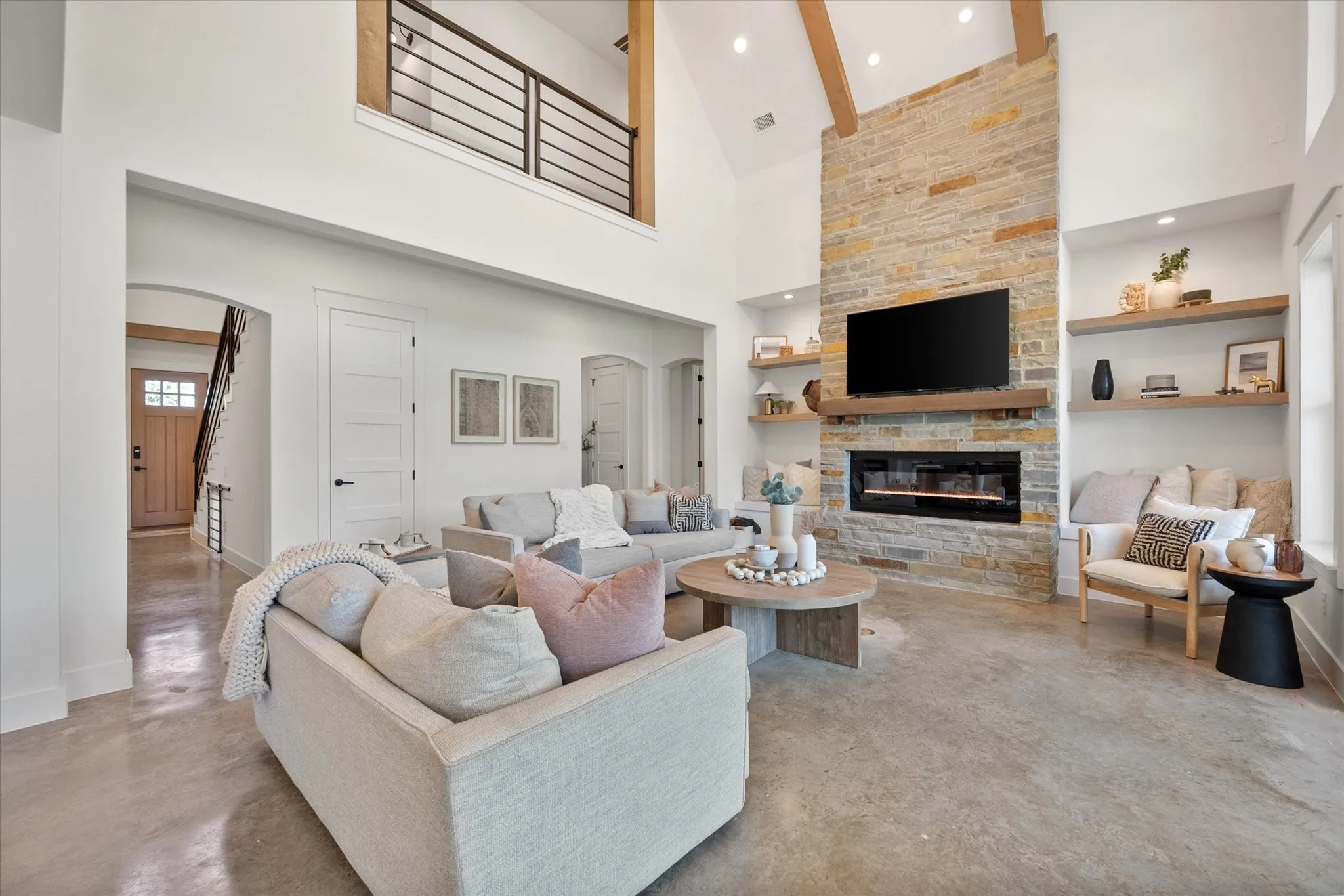 Living area featuring arched walkways, finished concrete flooring, high vaulted ceiling, built in shelves, and a stone fireplace