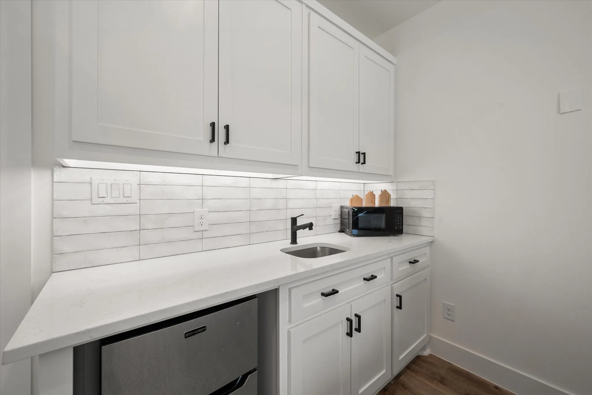 Bar featuring white cabinetry, light stone counters, backsplash, and black microwave