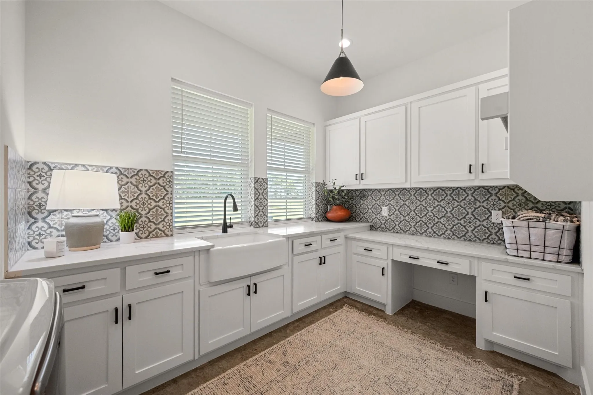 Kitchen with white cabinets, light stone counters, decorative light fixtures, and built in study area