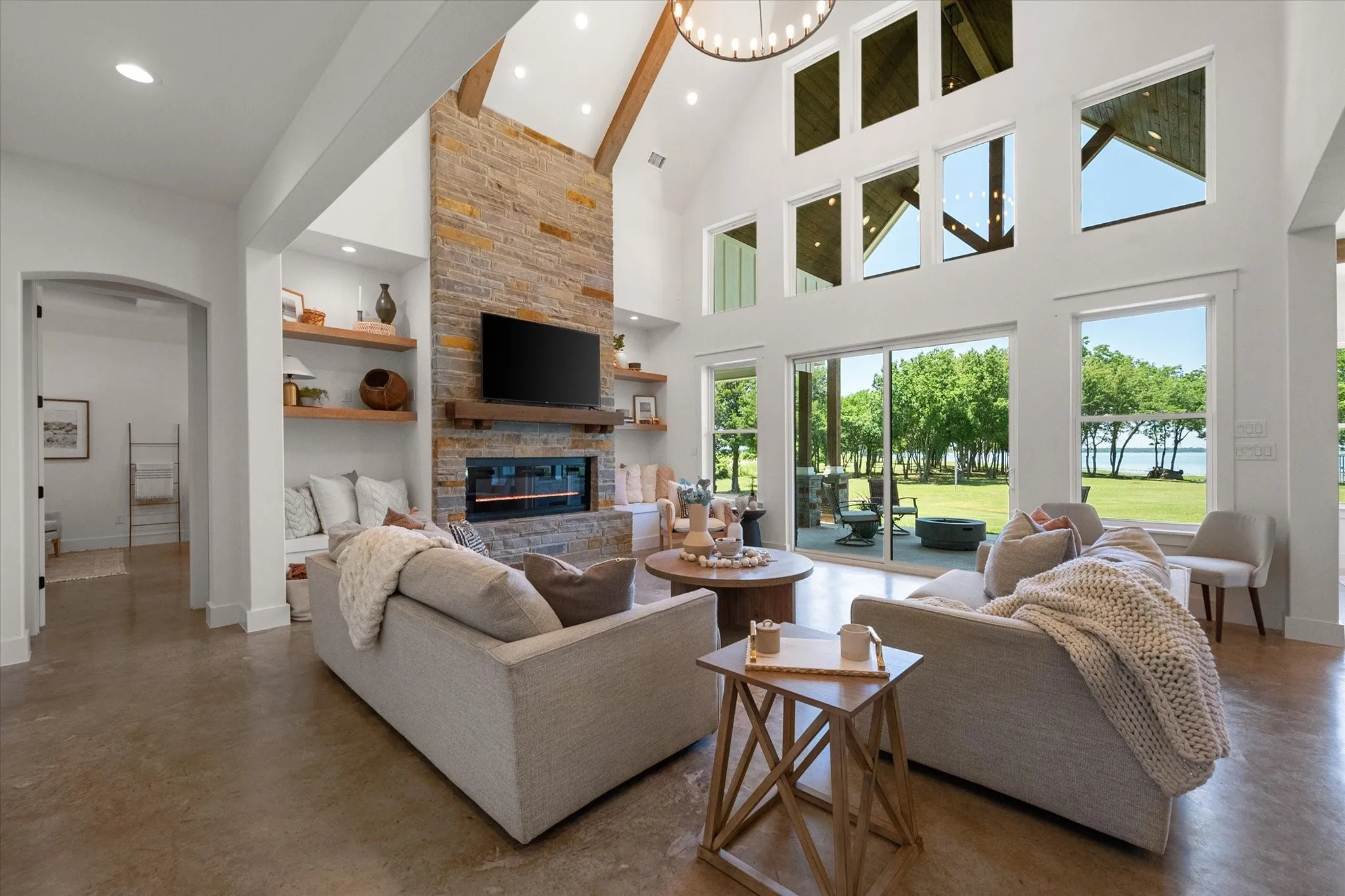 Living area with concrete flooring, built in shelves, a stone fireplace, arched walkways, and a towering ceiling