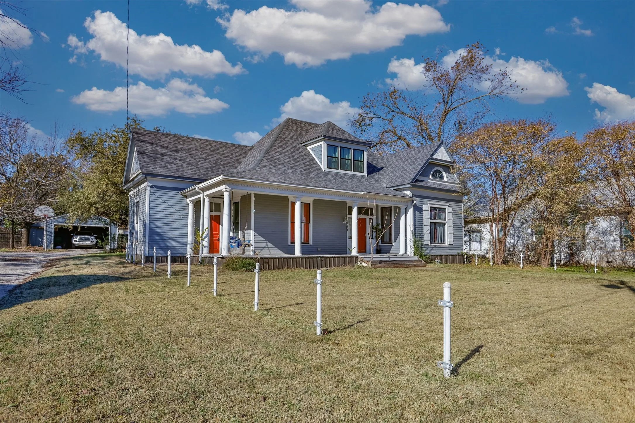 View of front facade featuring covered porch, a front lawn, a shingled roof, and a garage