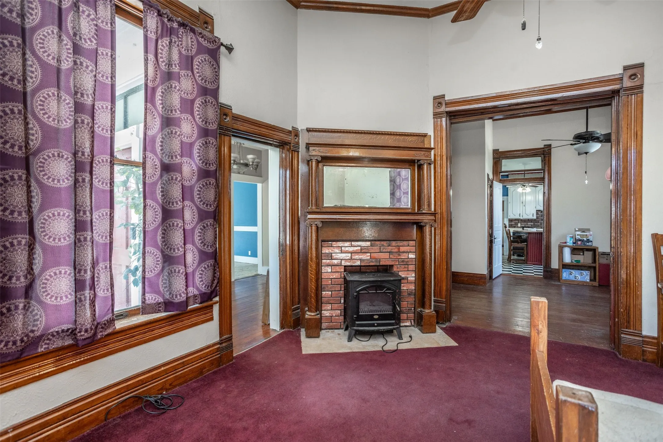 Carpeted living area with a ceiling fan, a decorative fireplace, a high ceiling, and crown molding