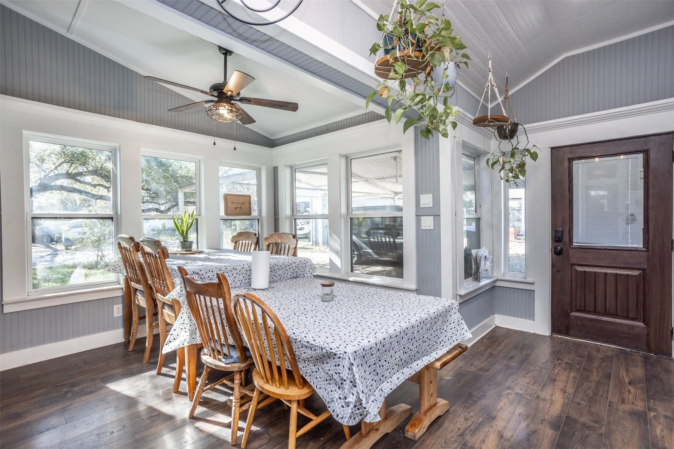 Dining room, lined with windows and with lofted ceiling, dark wood-style flooring, ceiling fan, and crown molding