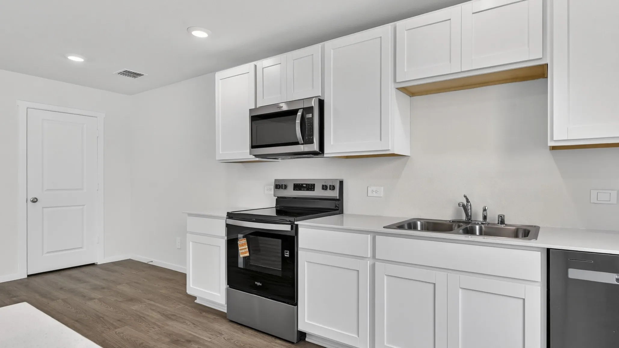 Kitchen featuring white shaker-style cabinetry, stainless steel appliances, light-toned countertops, and wood-finish flooring