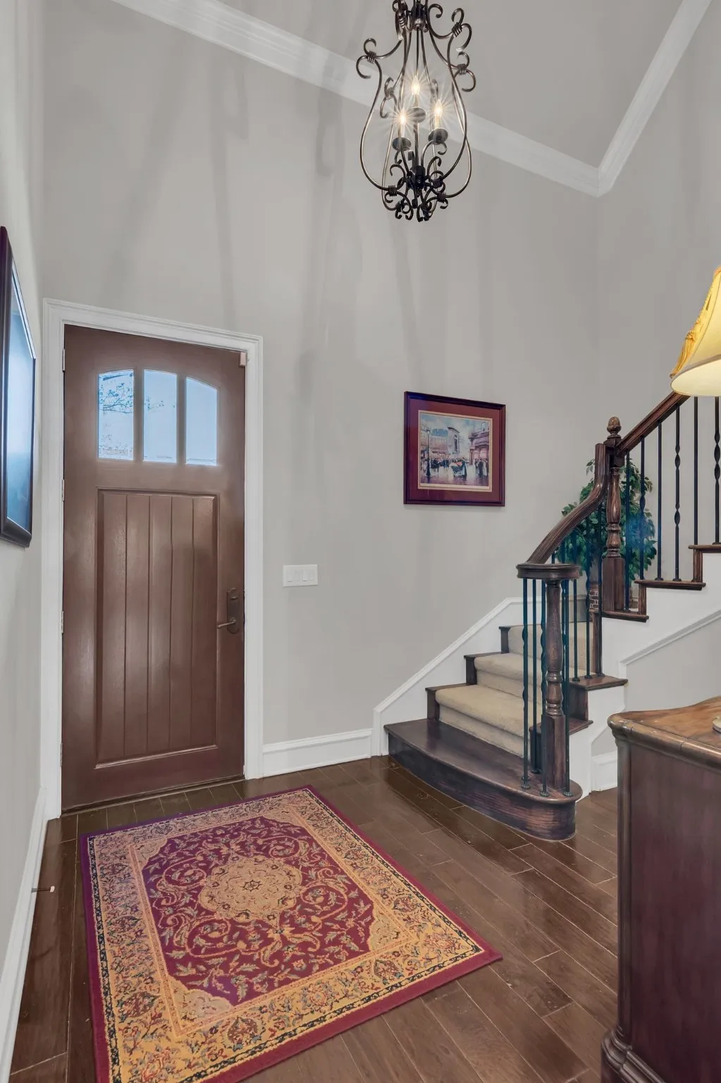 Entryway with crown molding, wood floors, stairs, and a chandelier