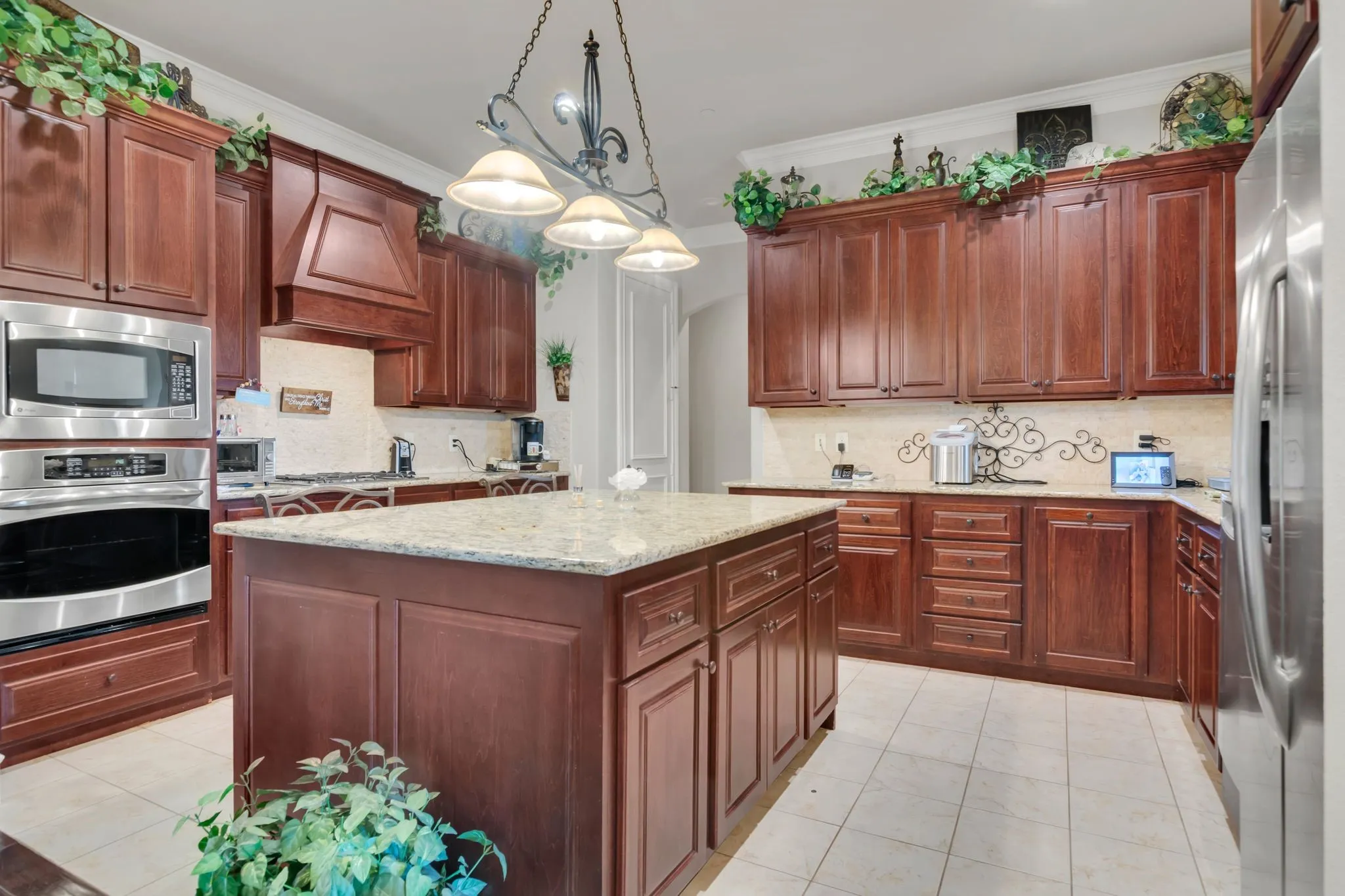 Kitchen featuring appliances with stainless steel finishes, hanging light fixtures, backsplash, light granite counters, and ornamental molding