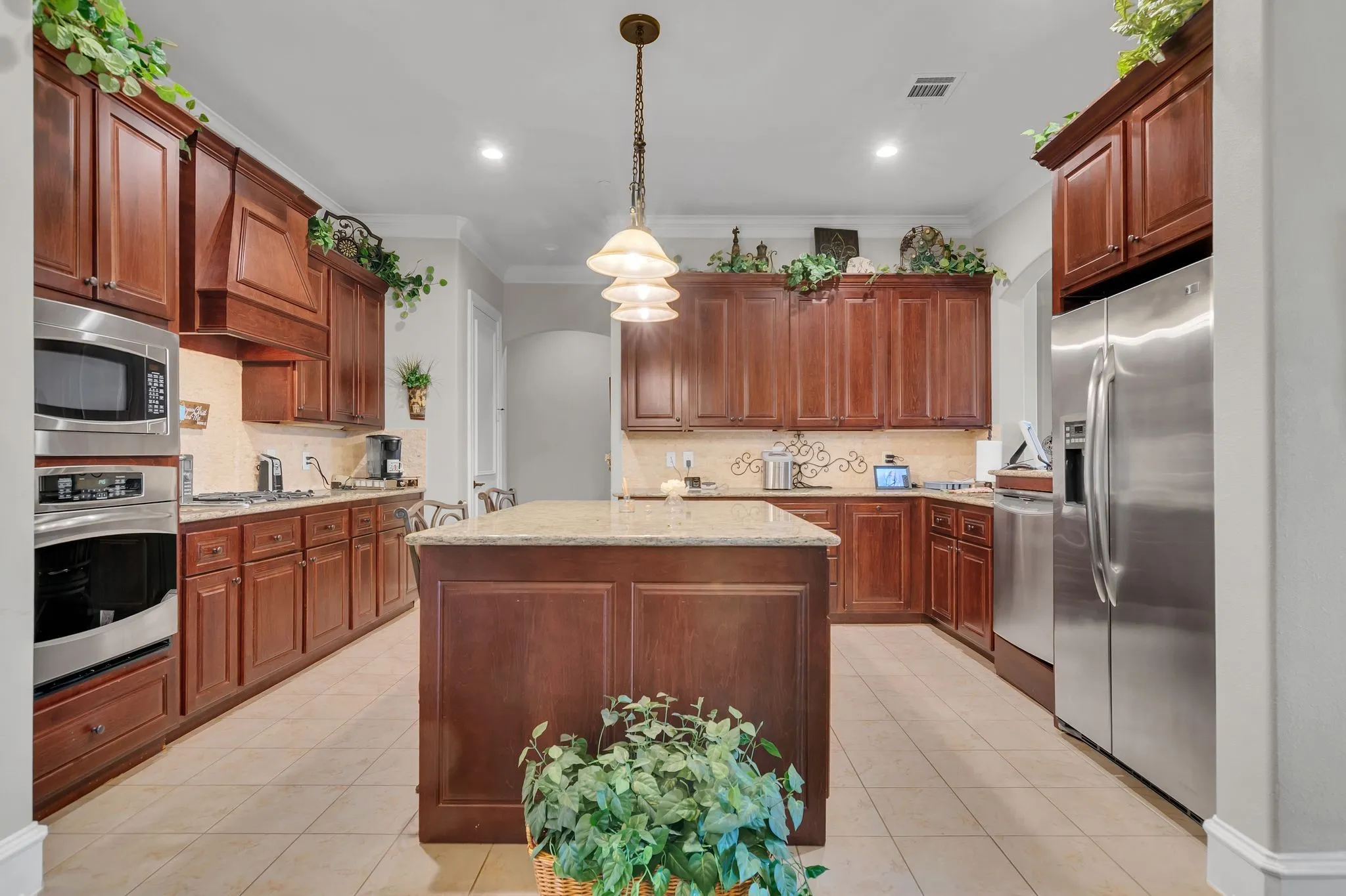 Kitchen featuring pendant lighting, stainless steel appliances, ornamental molding, light tile patterned flooring, and light granite counters