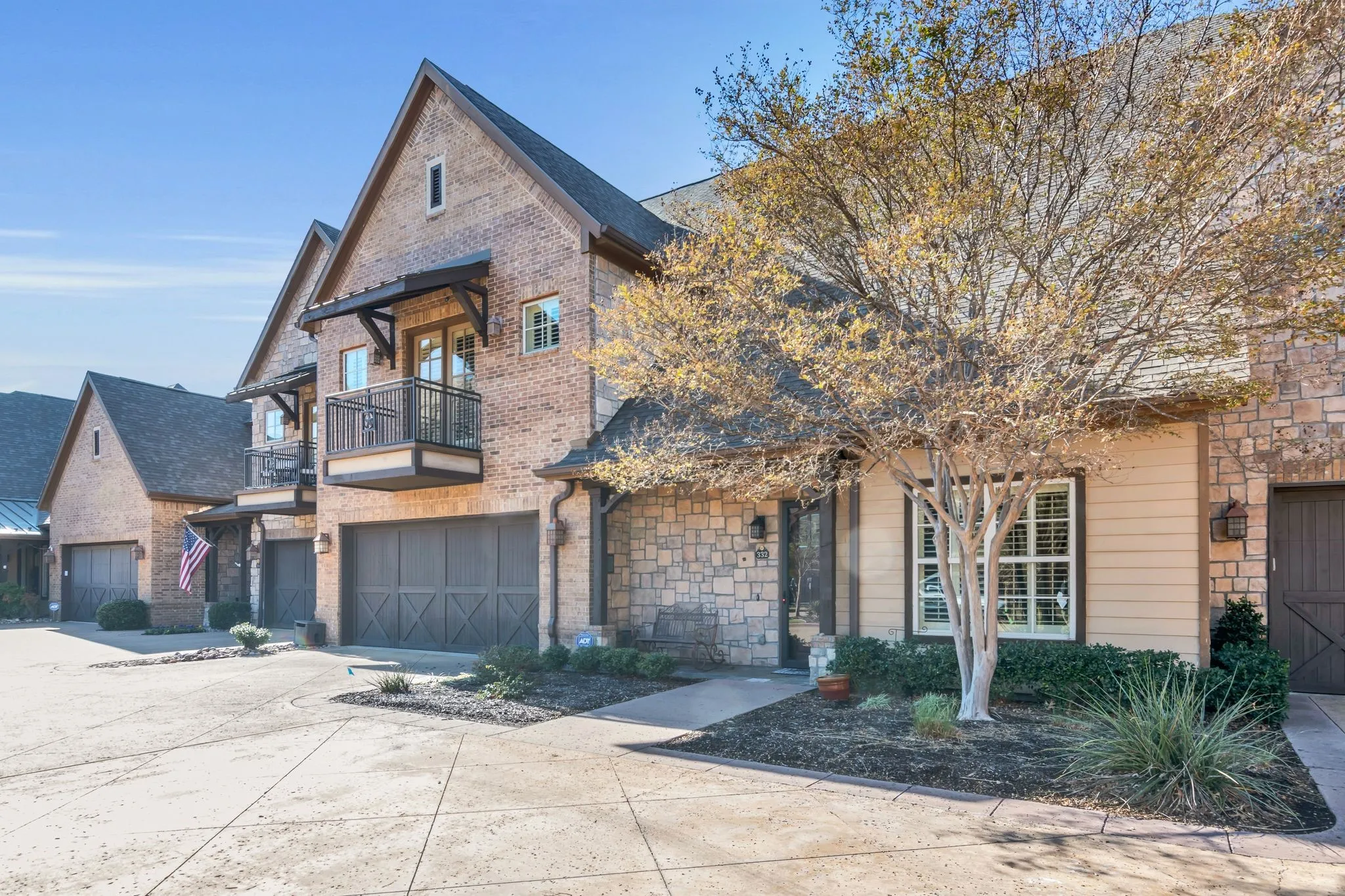 View of front of property featuring a balcony, driveway, an attached garage, brick siding, and roof with shingles
