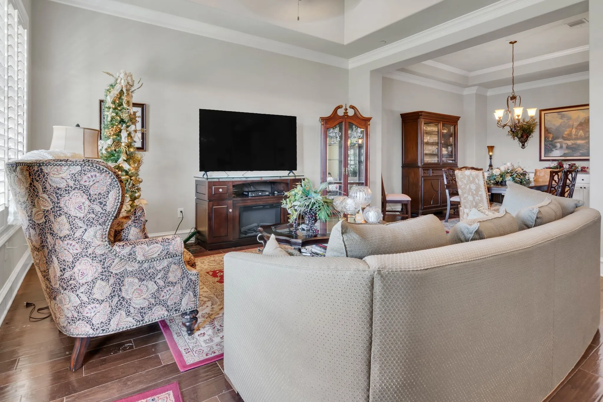 Living room featuring wood finish floors, a tray ceiling, a chandelier, and crown molding