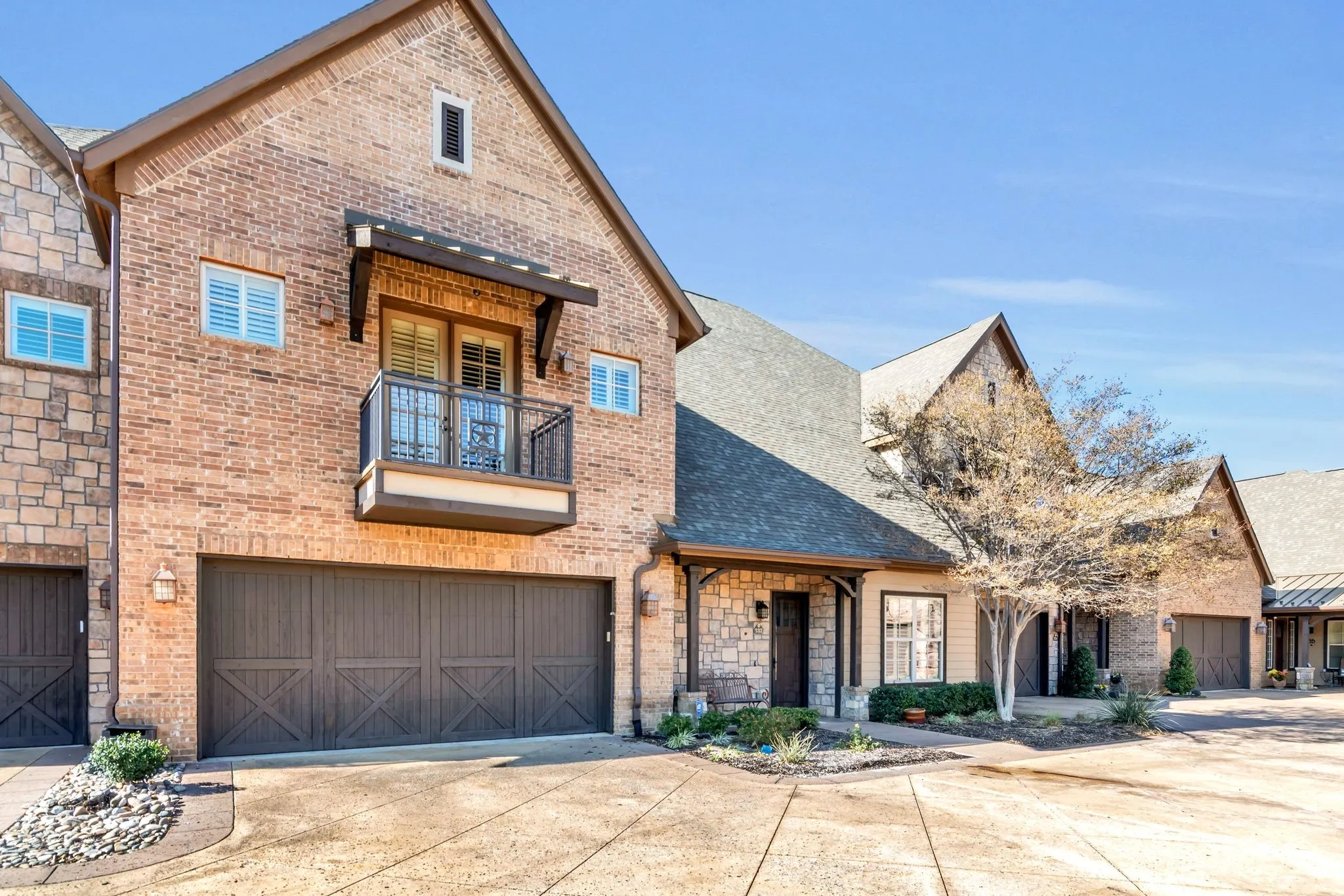 View of front facade with a balcony, driveway, brick siding, a shingled roof, and an attached garage