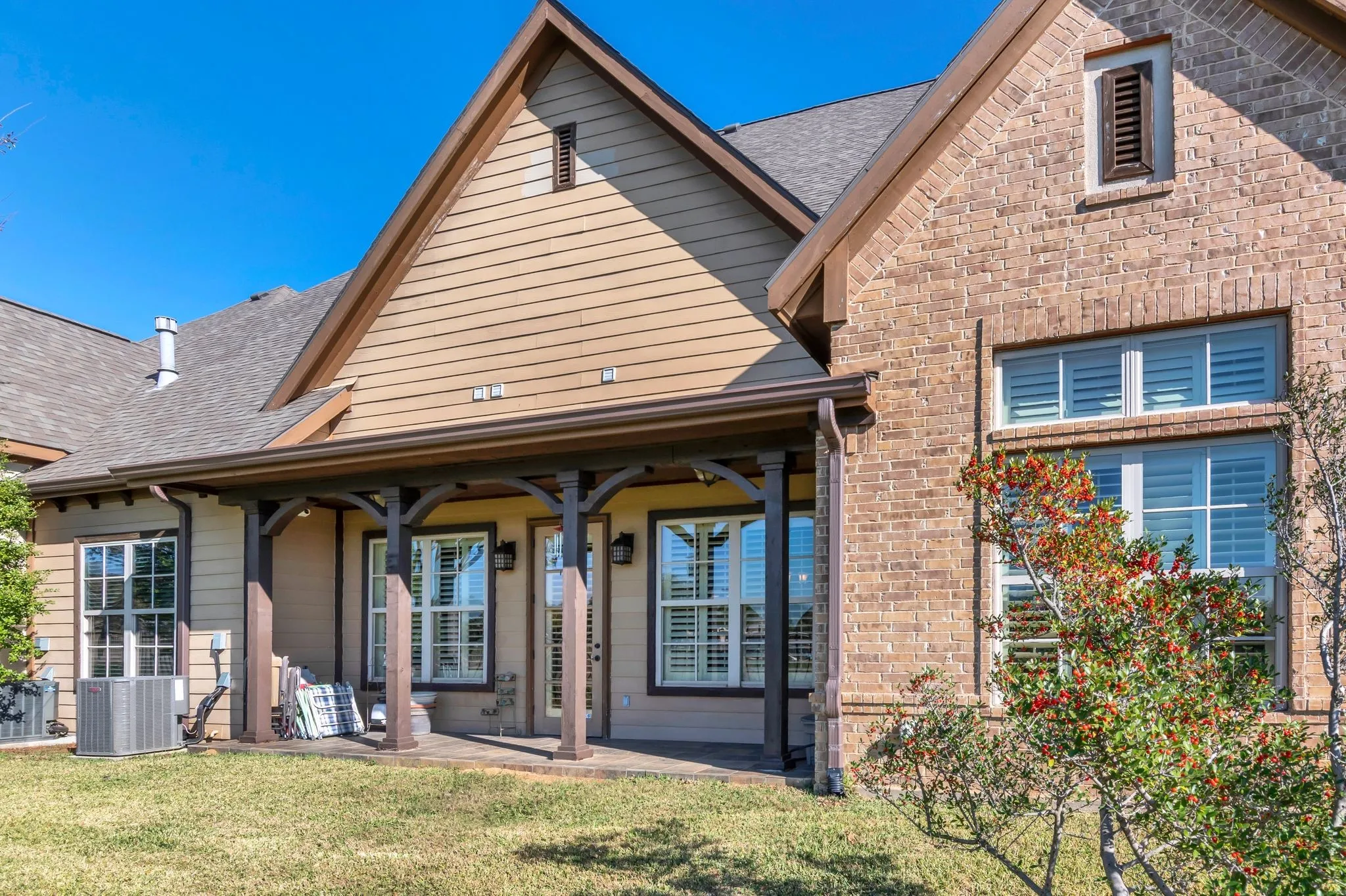 View of back of condo featuring a yard, roof with shingles, brick siding, and a patio