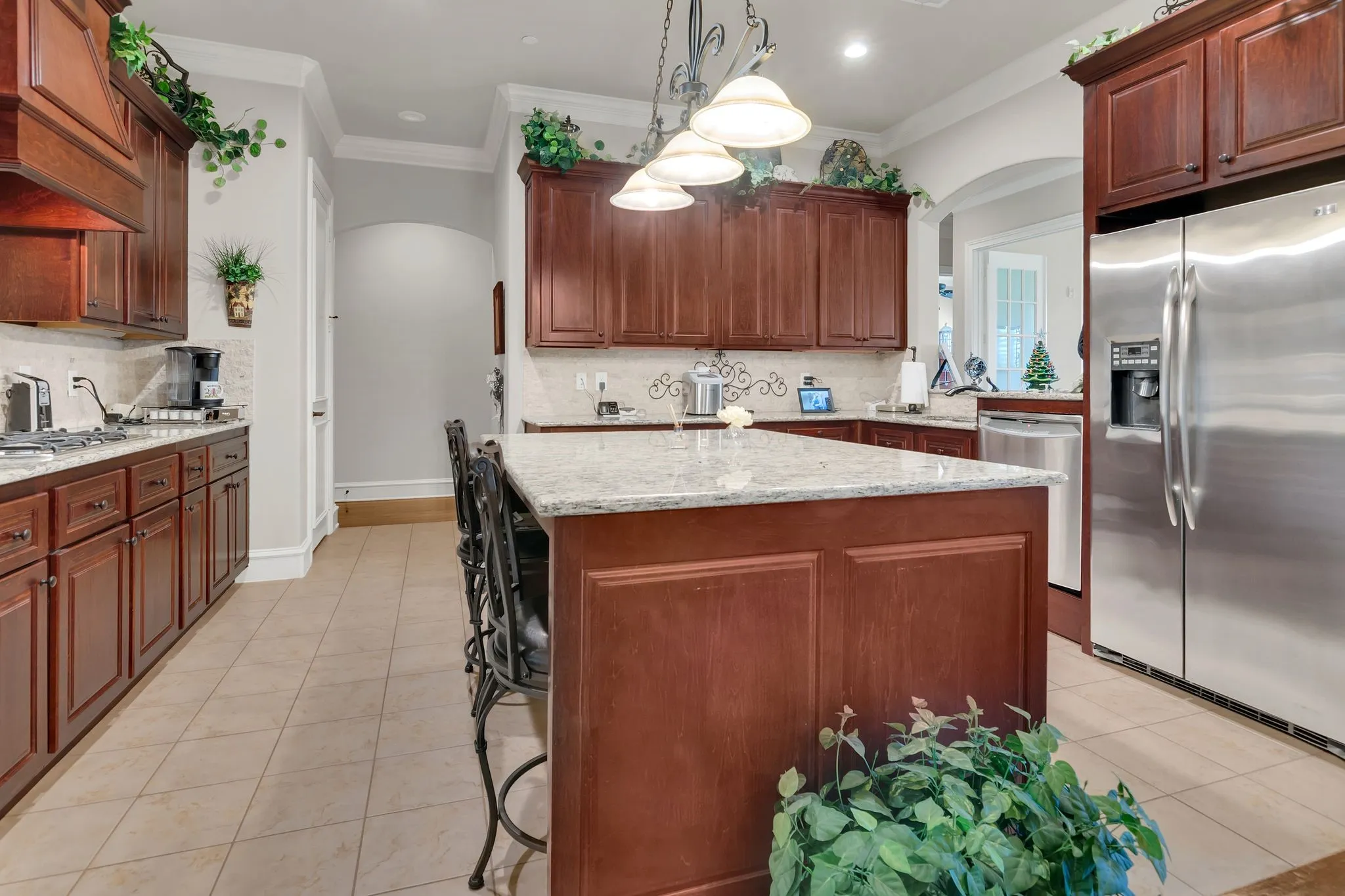 Kitchen featuring arched walkways, appliances with stainless steel finishes, hanging light fixtures, light granite counters, and a center island