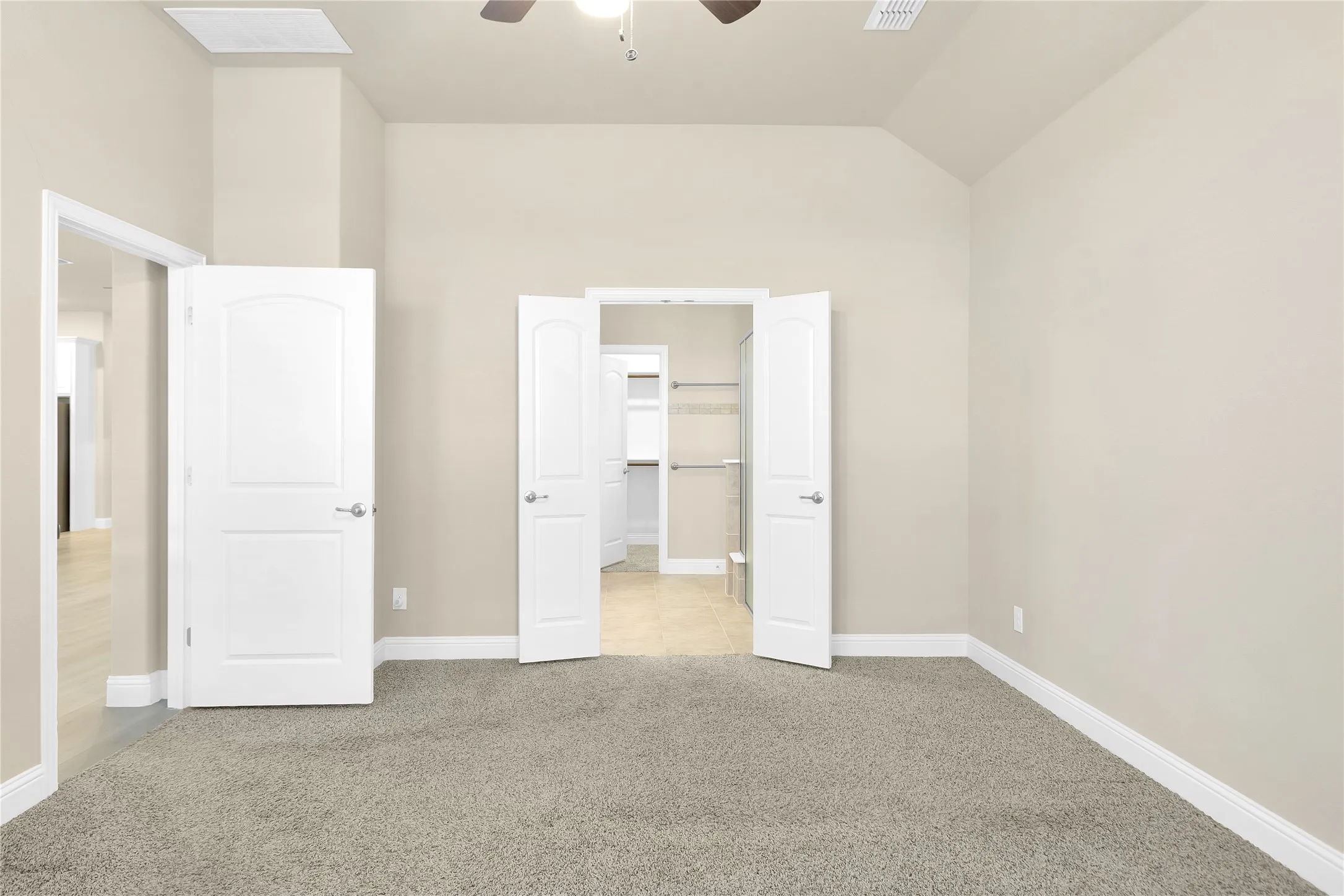 Master suite with light colored carpet, lofted ceiling, ceiling fan, and a walk in closet