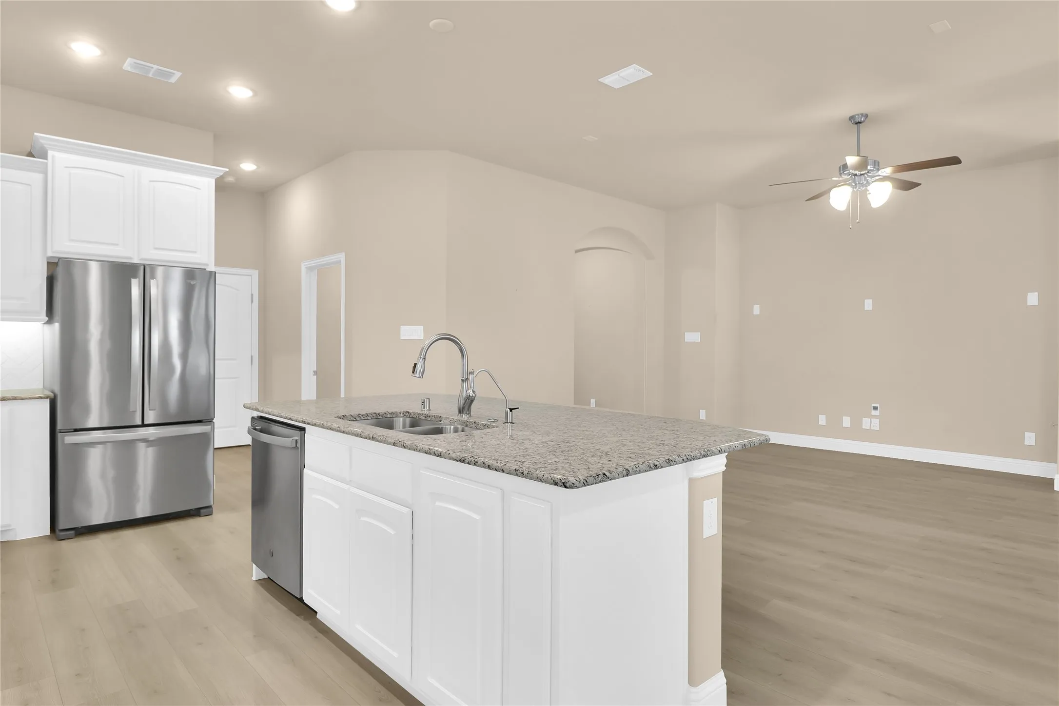 Kitchen with white cabinets, appliances with stainless steel finishes, light stone counters, arched walkways, and light luxury vinyl flooring. Fridge stays!