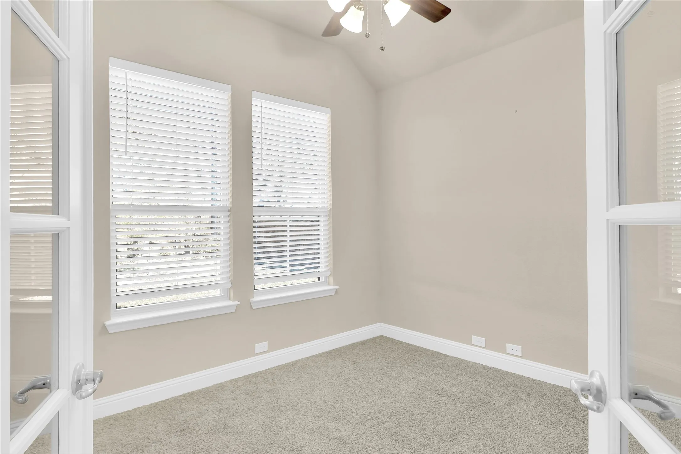 Carpeted office or spare bedroom featuring french doors, lofted ceiling, and a ceiling fan