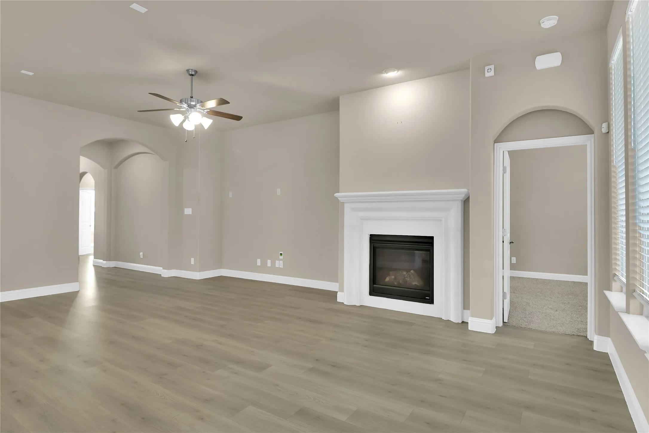 Living room with a glass covered gas fireplace, arched walkways, light wood finished floors, and ceiling fan
