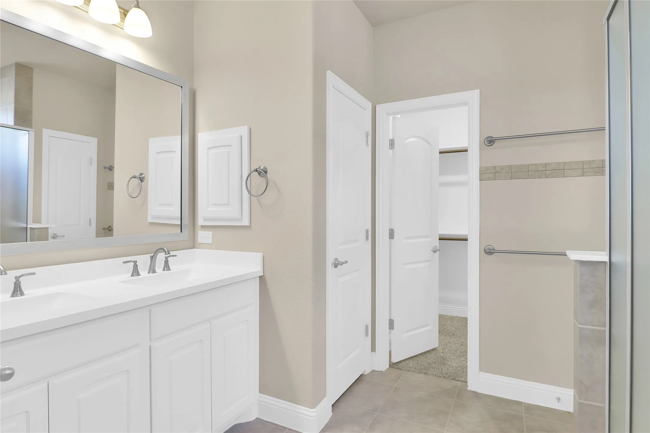 Bathroom featuring double vanity, a shower with door, a spacious closet, and light tile patterned flooring