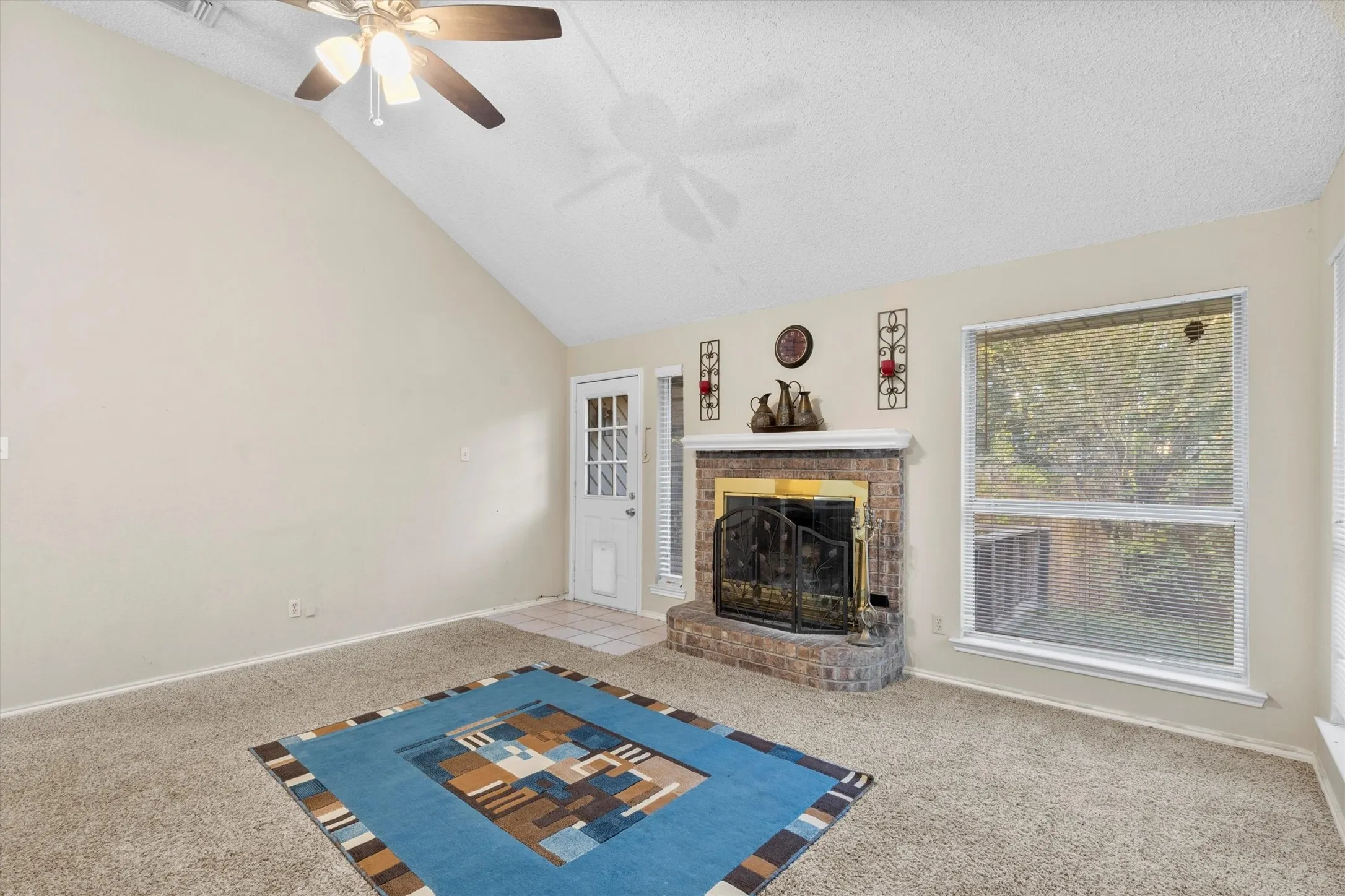 Unfurnished living room with carpet flooring, a textured ceiling, a brick fireplace, ceiling fan, and high vaulted ceiling