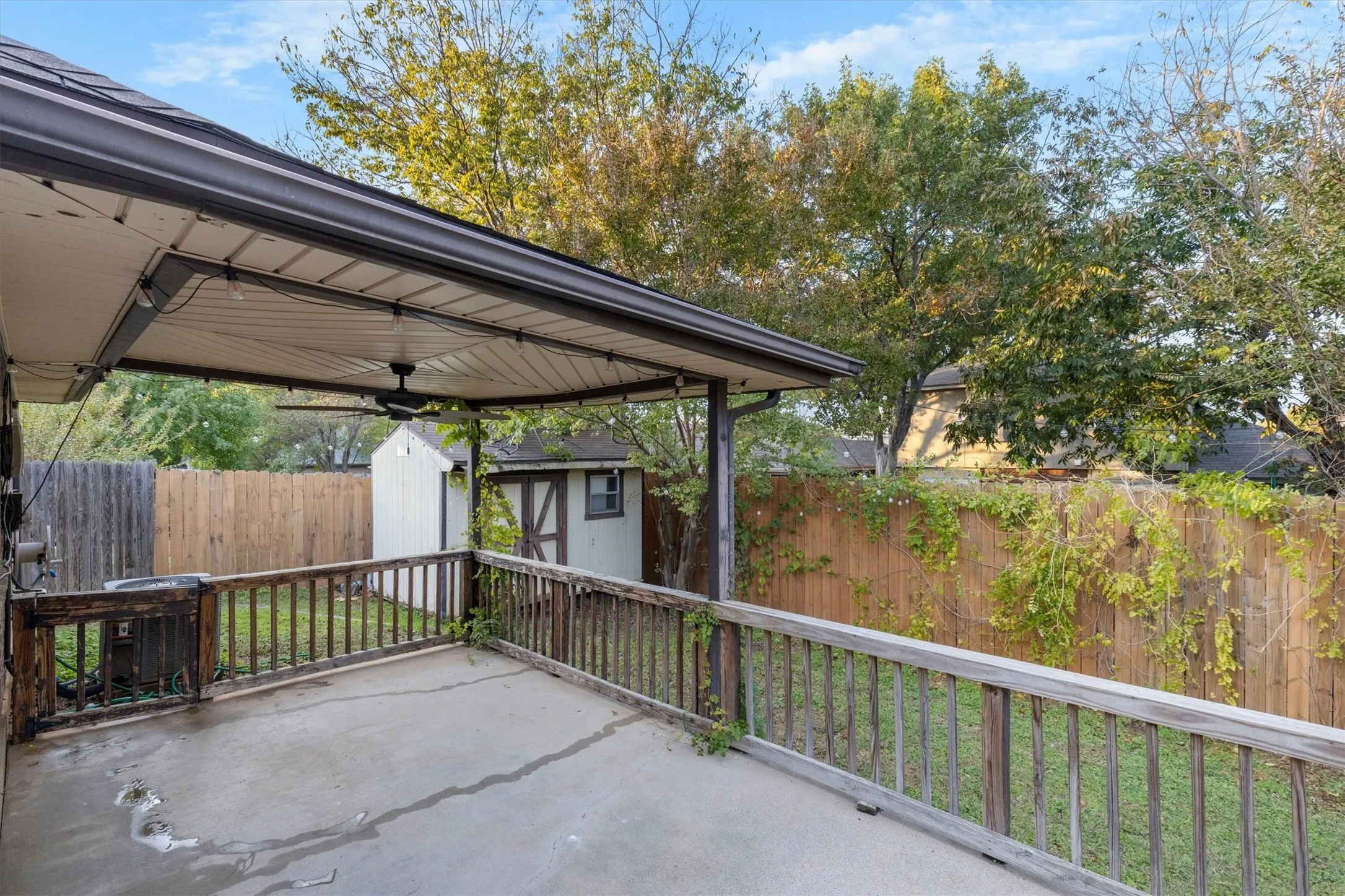 Fenced backyard featuring a storage unit, a ceiling fan, and a patio