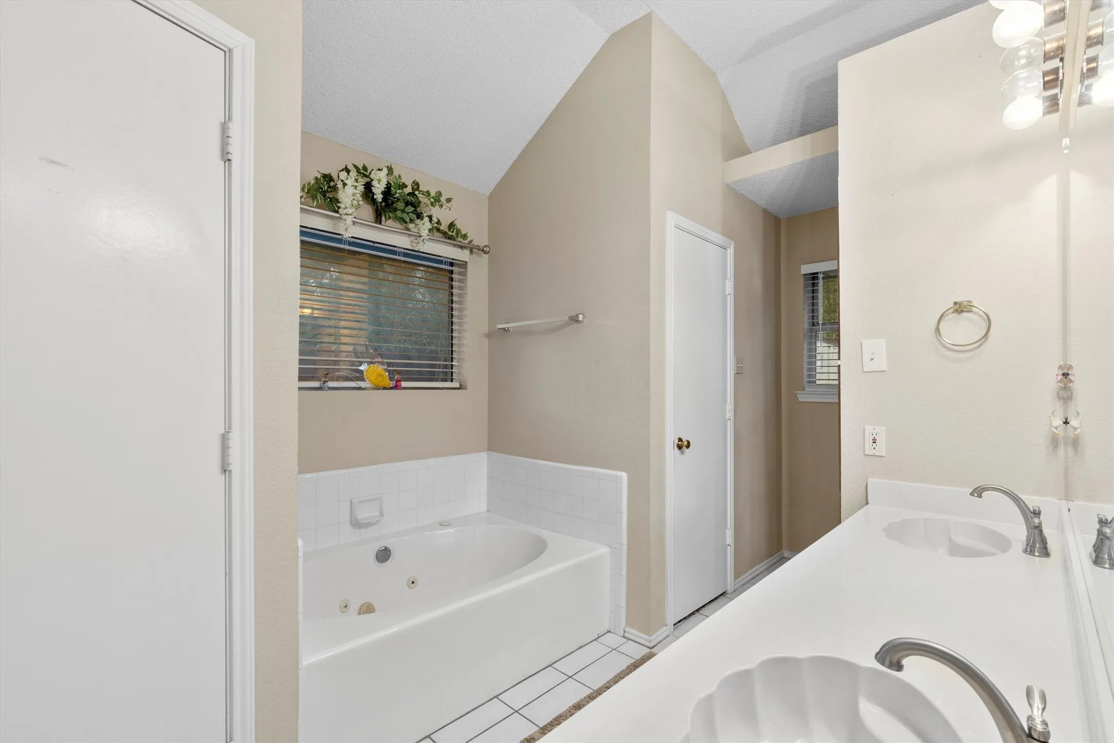 Bathroom featuring tile patterned floors, a jetted tub, double vanity, and vaulted ceiling