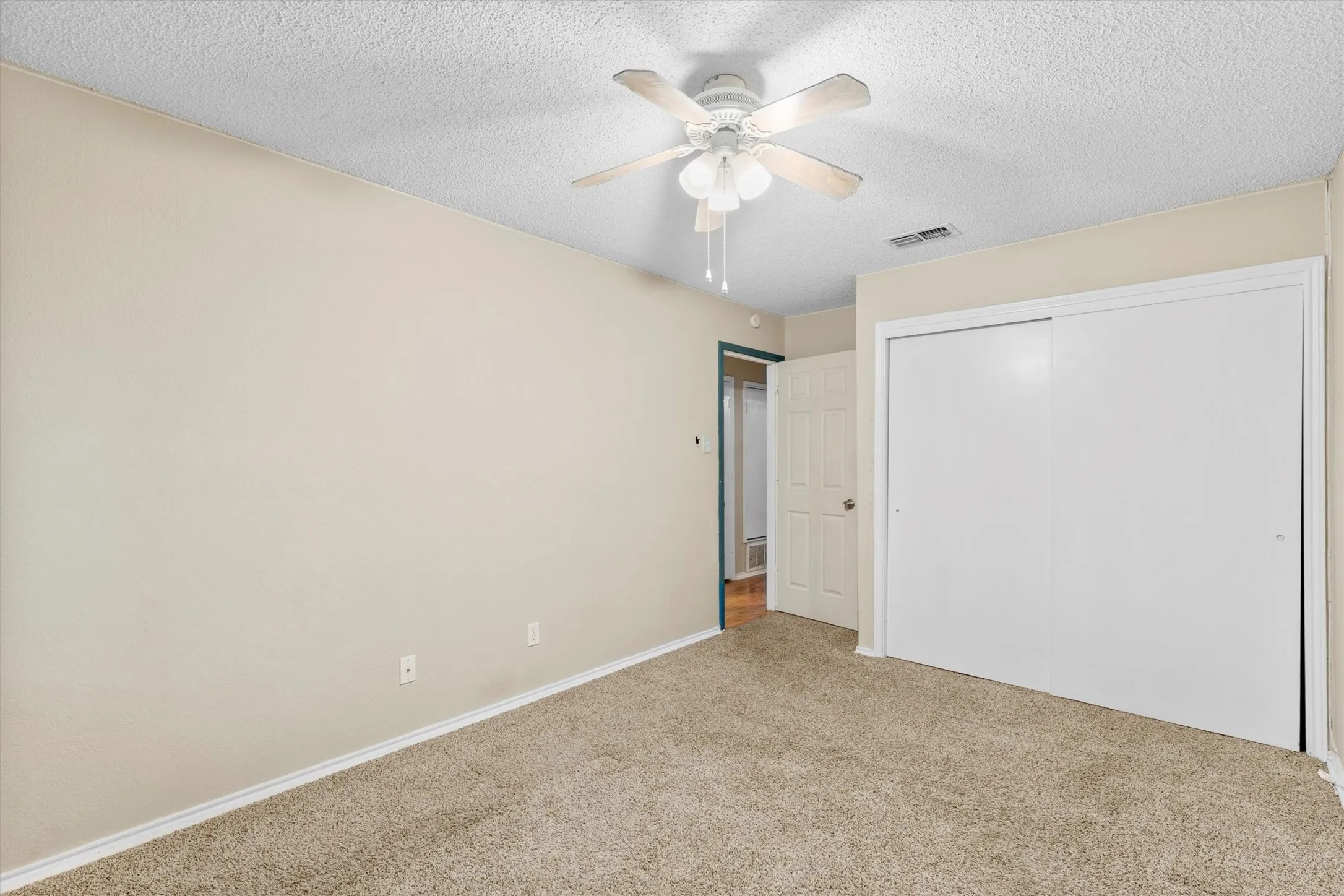 Unfurnished bedroom featuring carpet, a textured ceiling, a closet, and a ceiling fan