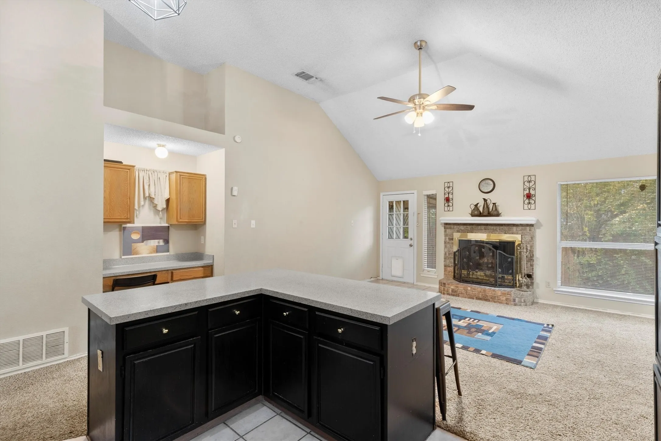 Kitchen with dark cabinetry, light carpet, a center island, light countertops, and vaulted ceiling