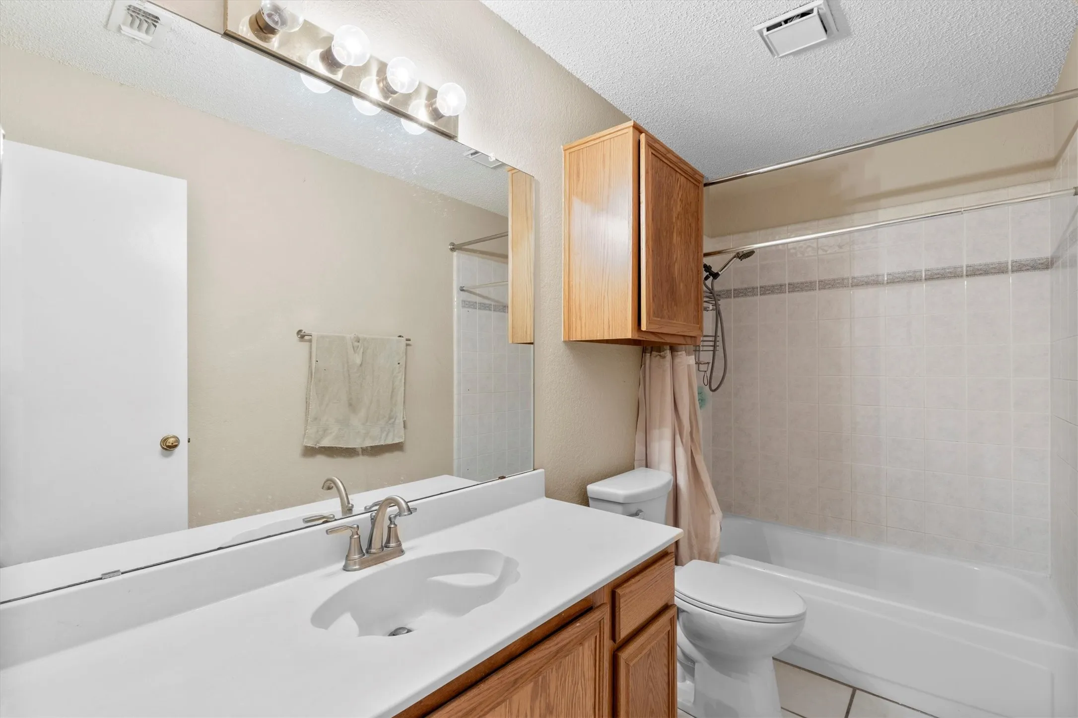 Full bath with vanity, shower / tub combo, a textured ceiling, and tile patterned floors