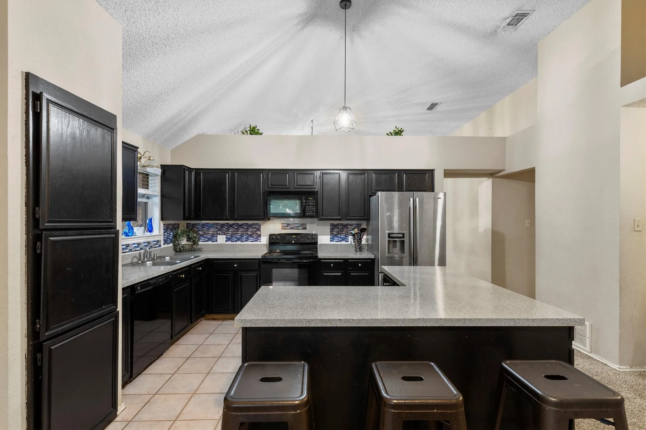 Kitchen with dark cabinetry, black appliances, a breakfast bar, a textured ceiling, and decorative backsplash