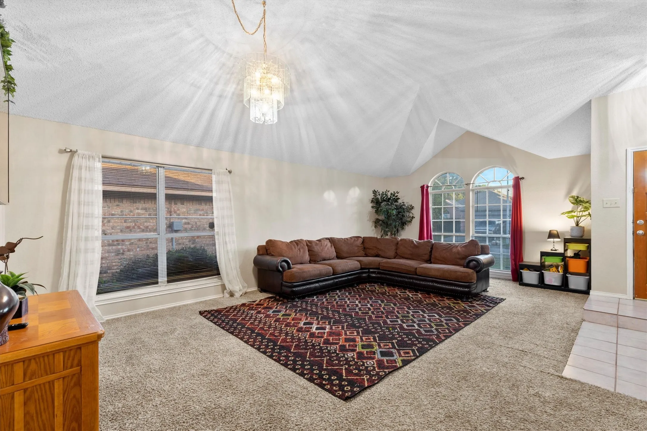 Living room with vaulted ceiling, light carpet, and a chandelier