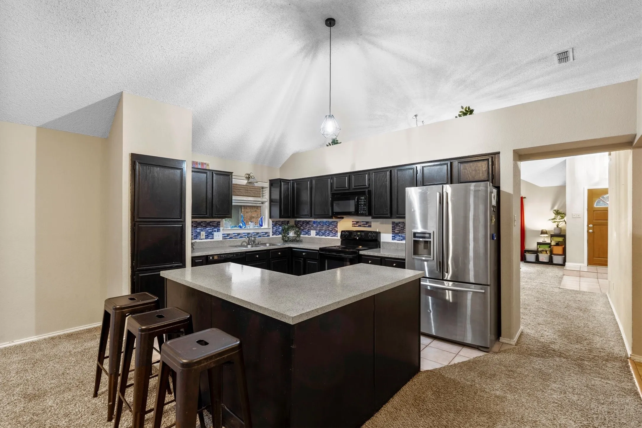 Kitchen featuring black appliances, lofted ceiling, light countertops, a textured ceiling, and a kitchen island
