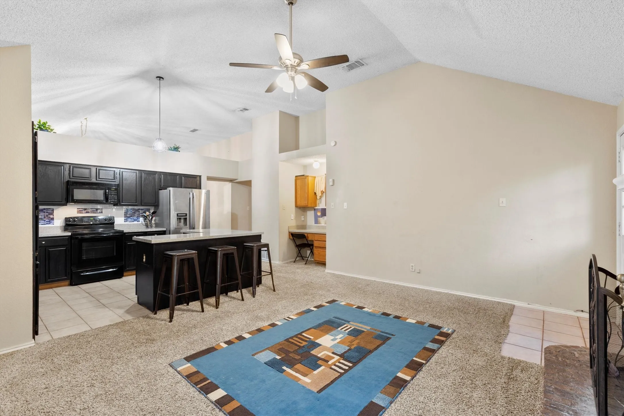 Living room featuring a ceiling fan, light tile patterned floors, light colored carpet, lofted ceiling, and a textured ceiling