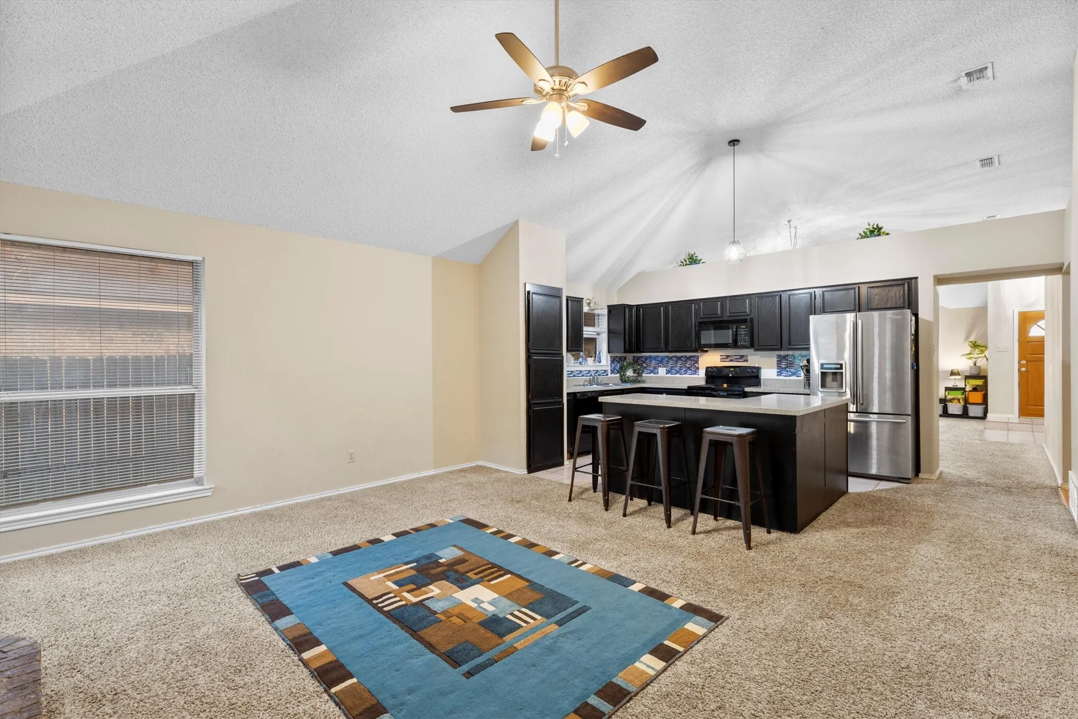 Kitchen with vaulted ceiling, light carpet, black appliances, dark cabinets, and a textured ceiling