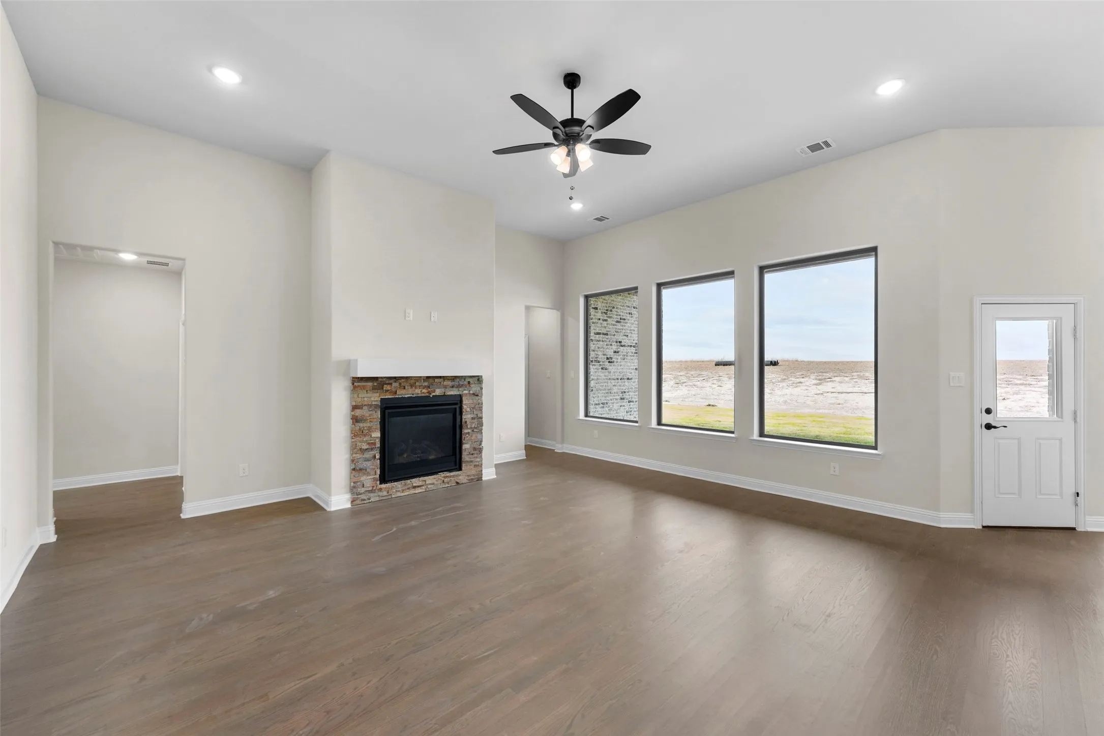 Wood-finish flooring, recessed lighting, and a stacked stone fireplace with a white mantle