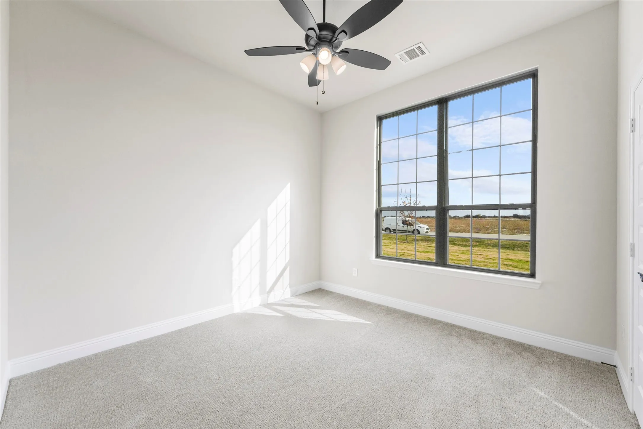 Recessed lighting, ceiling fan with integrated light, large multi-pane window, light-toned carpeting, and a white interior door