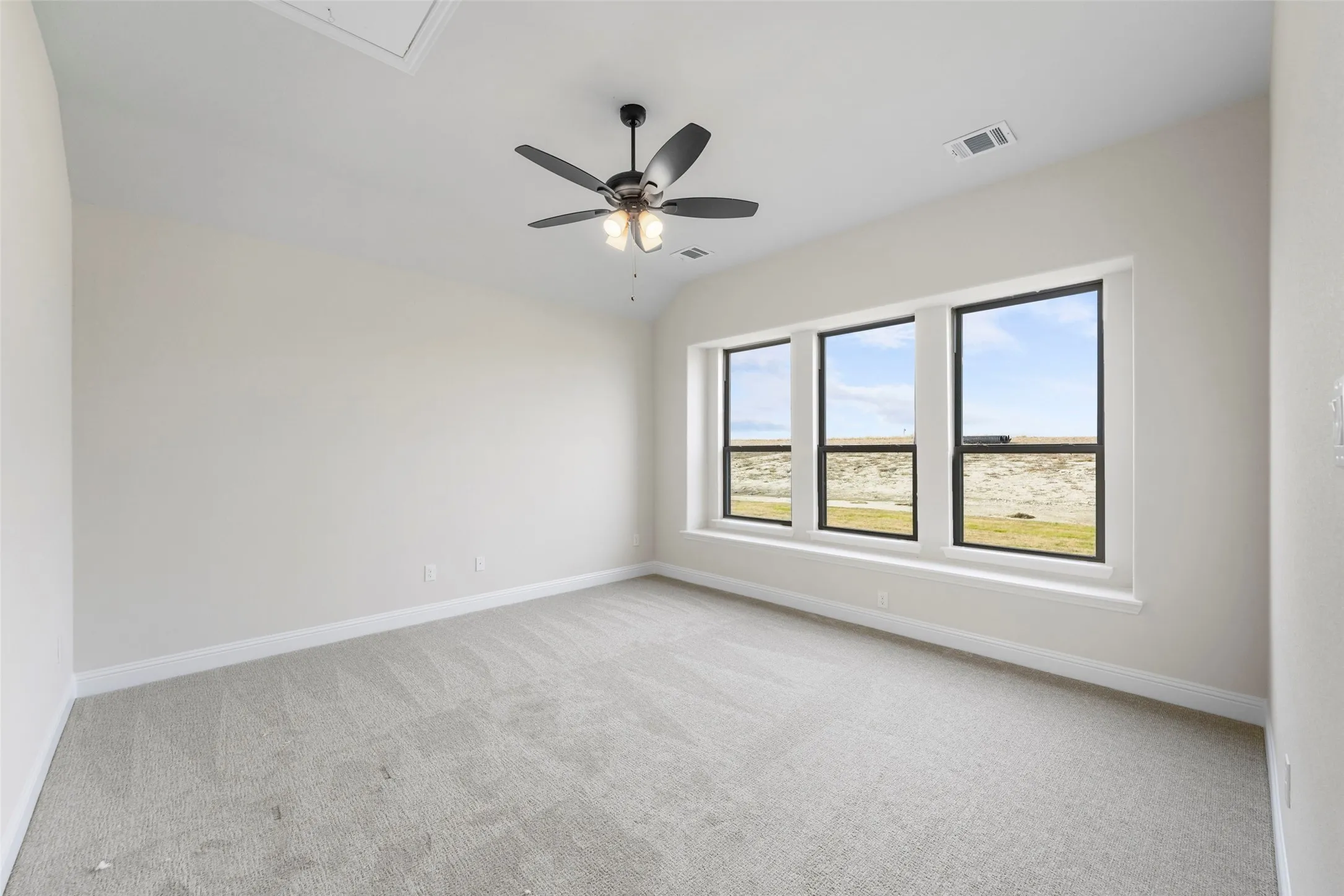 Vaulted ceiling, ceiling fan with integrated lighting, three large windows, light neutral wall color, and light grey carpeting