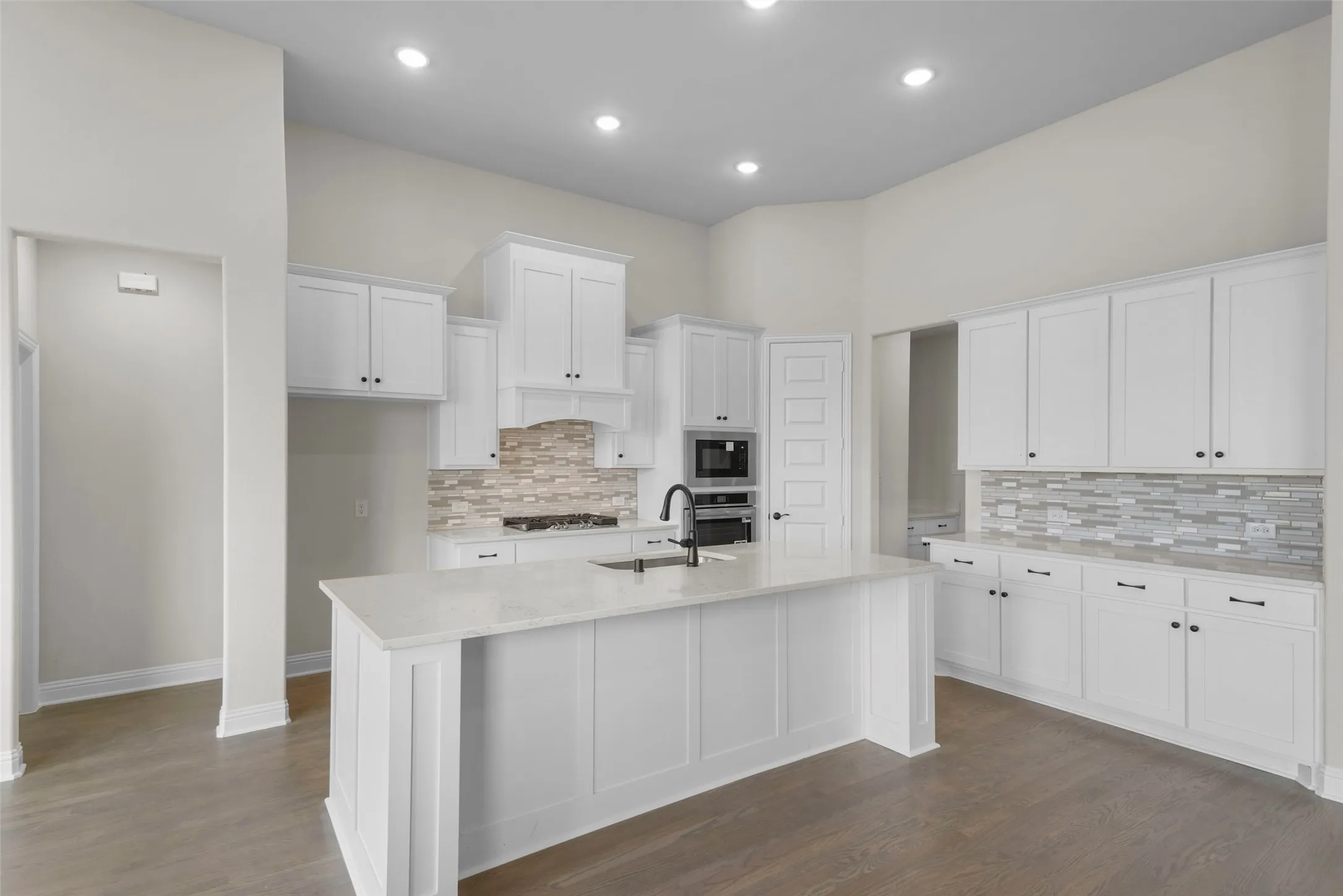 Bright kitchen featuring white shaker cabinetry, an expansive center island with an undermount sink, recessed lighting, and wood-finish flooring