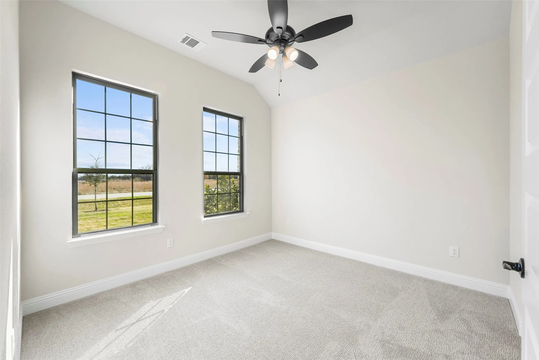 Vaulted ceiling with an attached ceiling fan, dual grid-pattern windows, and light-toned wall-to-wall carpeting