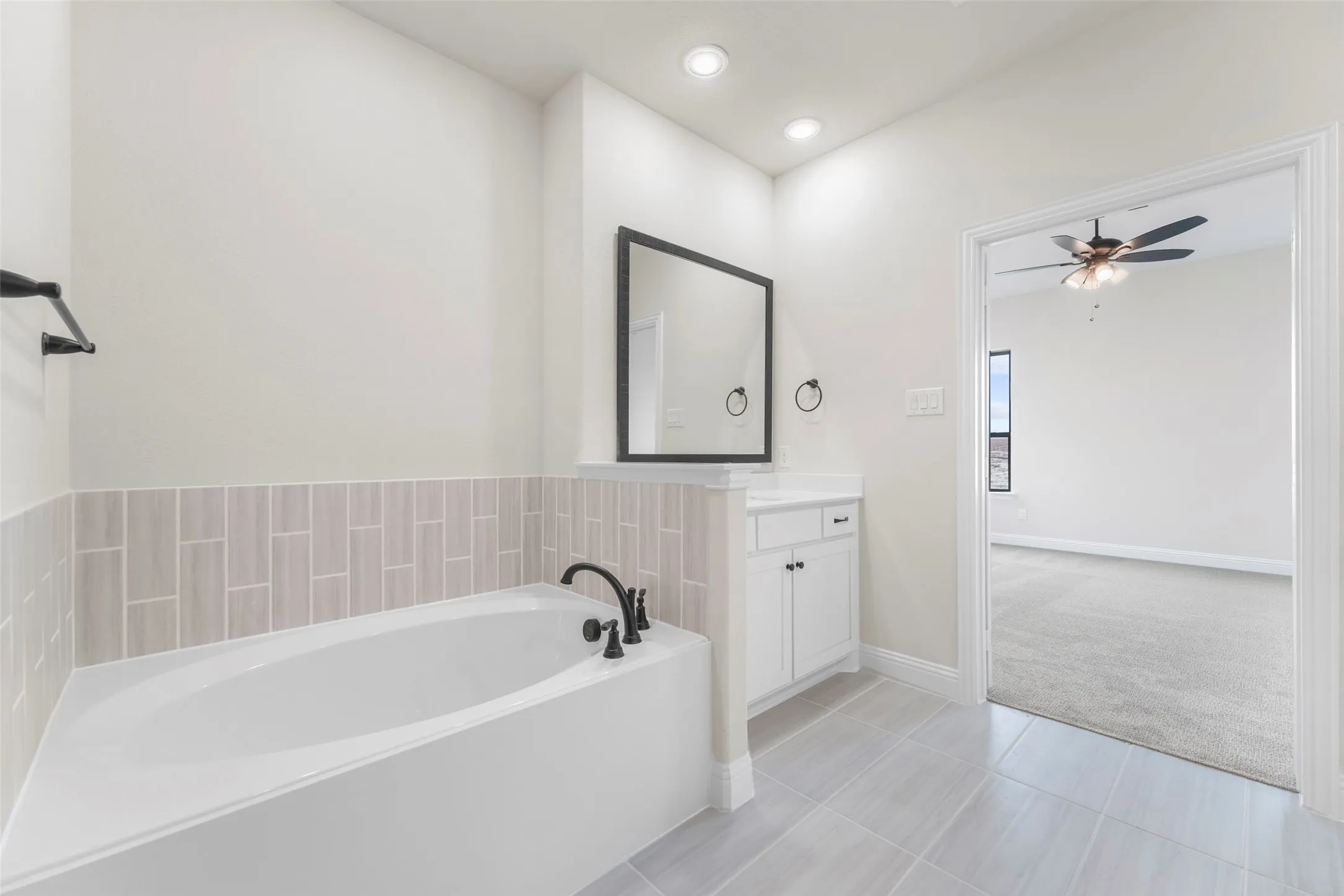 Built-in bathtub with black fixtures, vanity with storage, recessed lighting, and tile flooring
