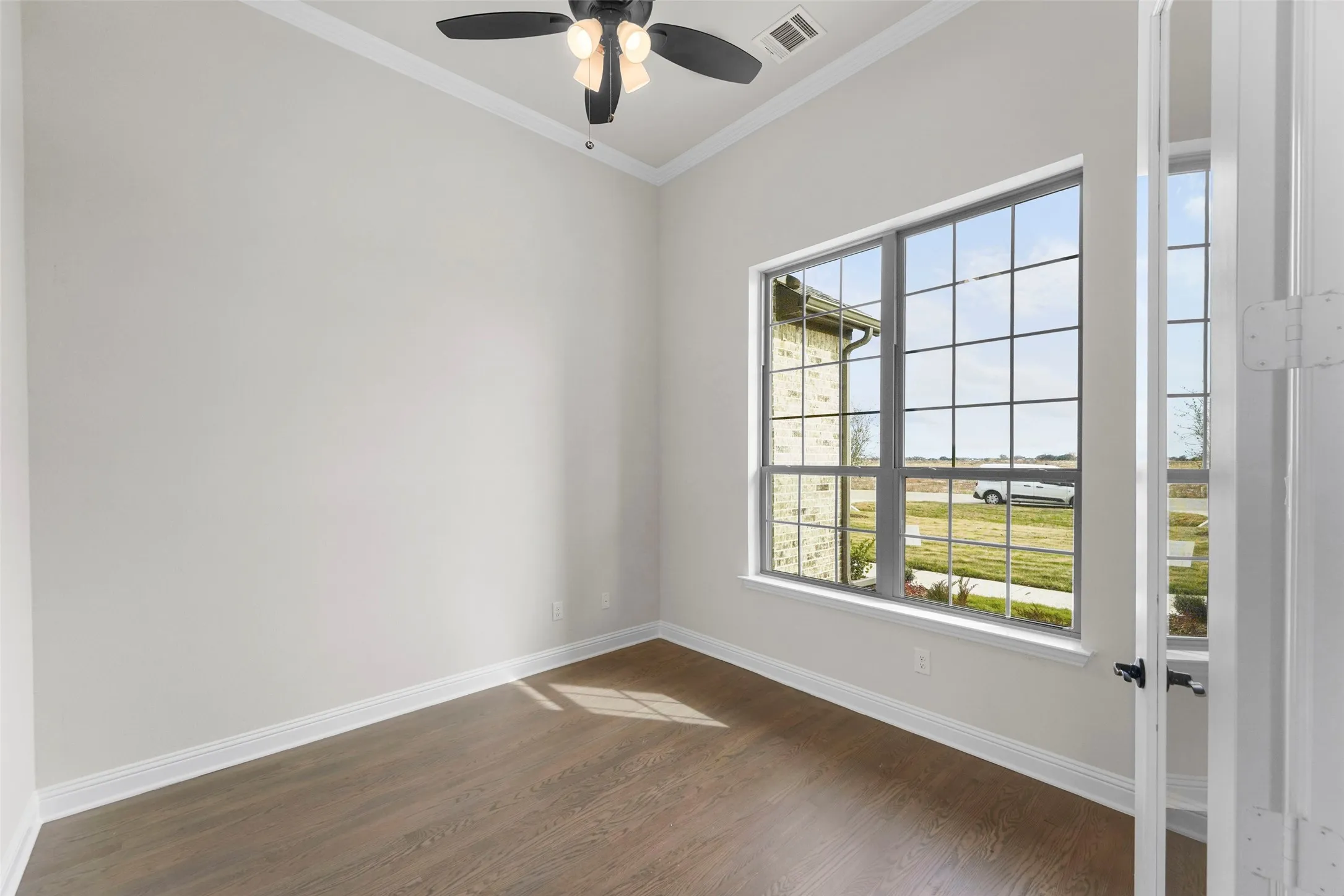 Vaulted ceiling with crown molding, wood-finish flooring, and a multi-pane window