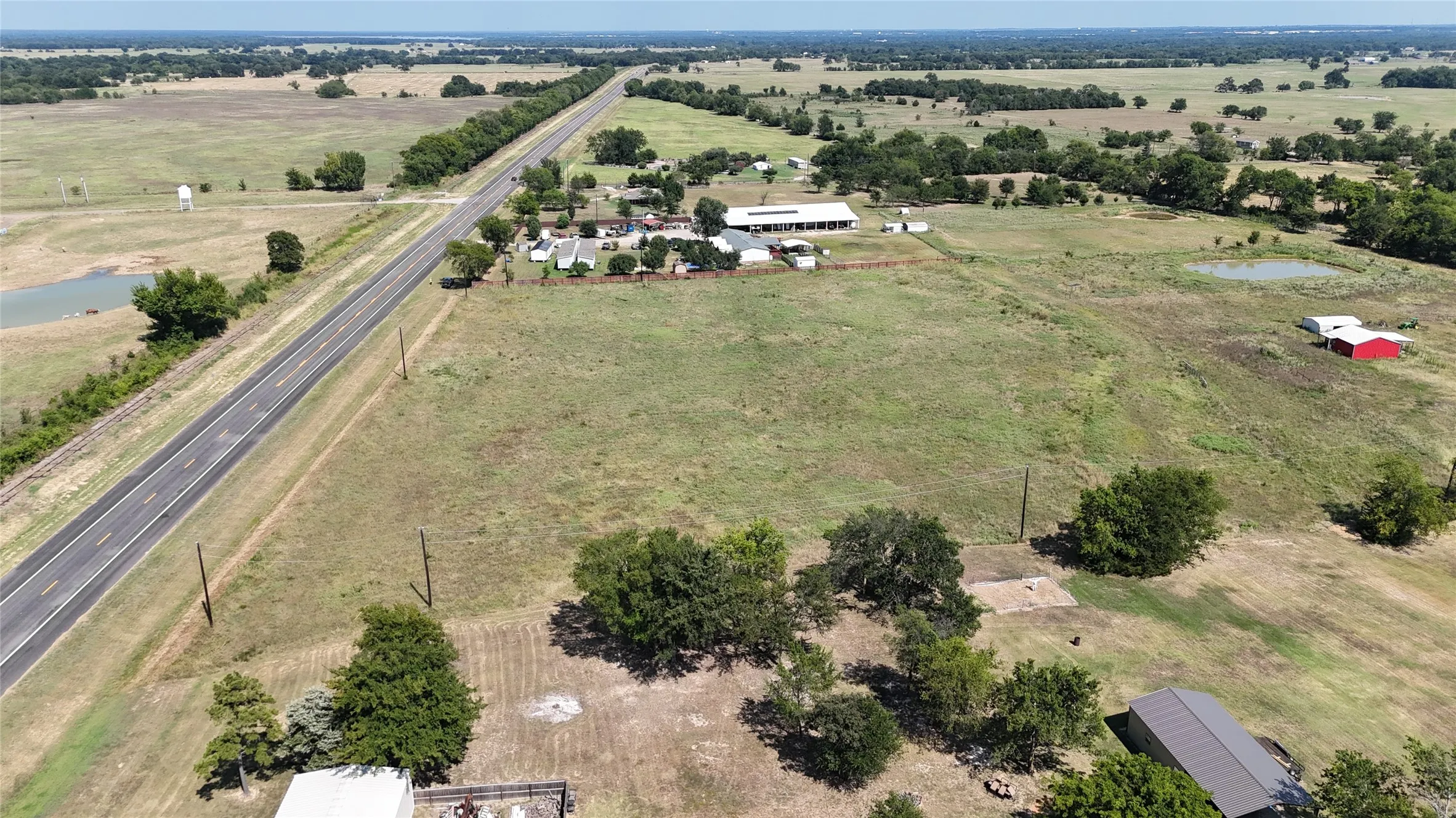 Expansive rural property featuring a two-lane paved road, multiple outbuildings, and scattered mature trees