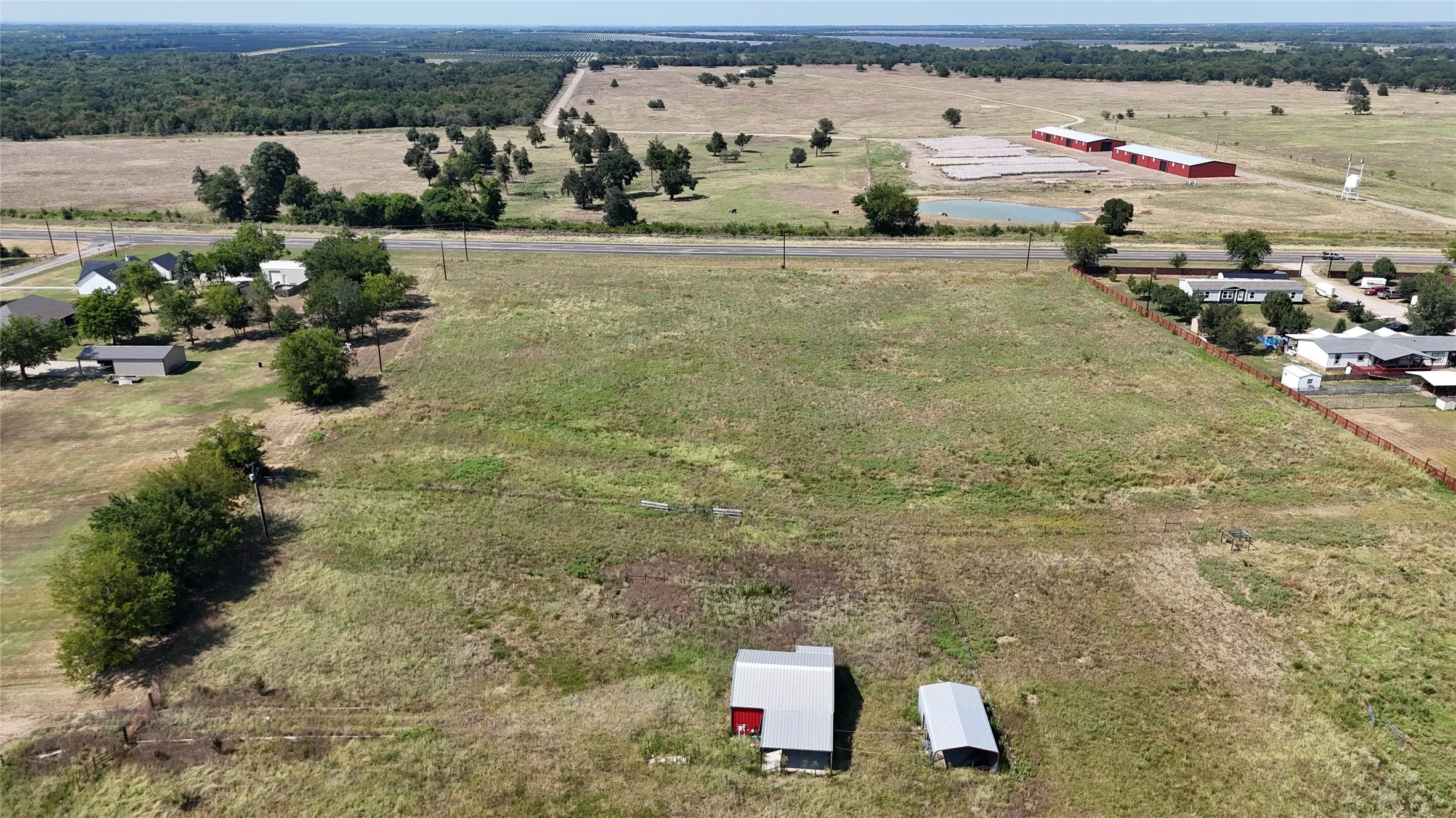 Expansive undeveloped land parcel featuring a metal-sided building with a red roof, a separate metal outbuilding, and direct road frontage