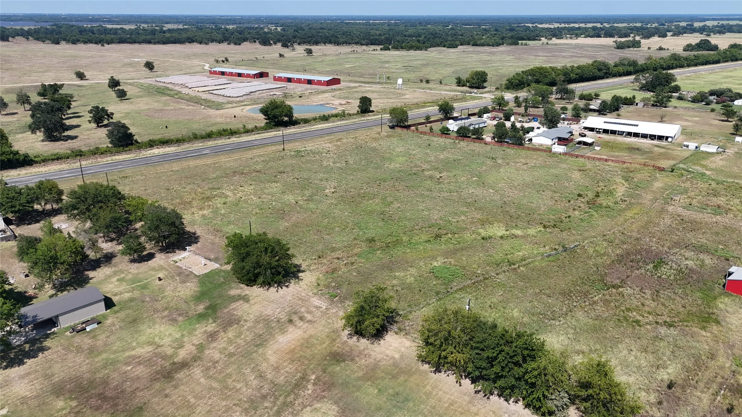 Expansive rural acreage with scattered trees, featuring a paved road frontage