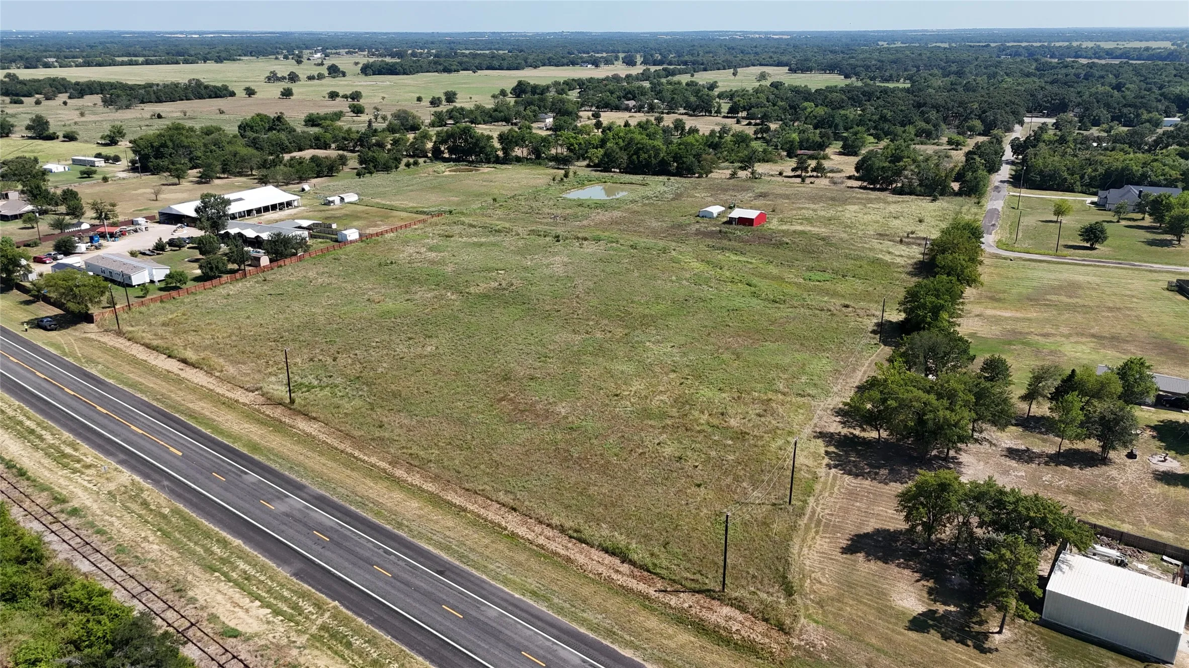Expansive rural acreage featuring open pastureland with mature tree lines, direct highway frontage, and multiple outbuildings including barns and agricultural structures